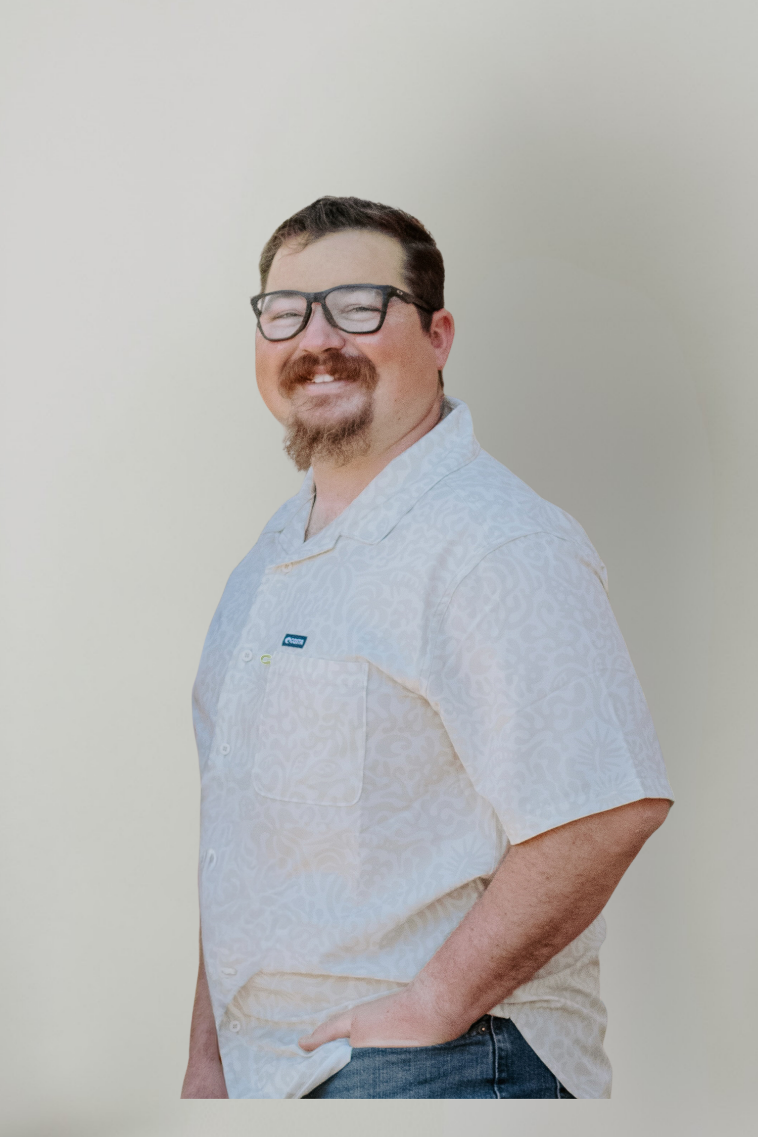 Smiling man with glasses and goatee wearing a light gray button-up shirt, posing confidently against a neutral background.