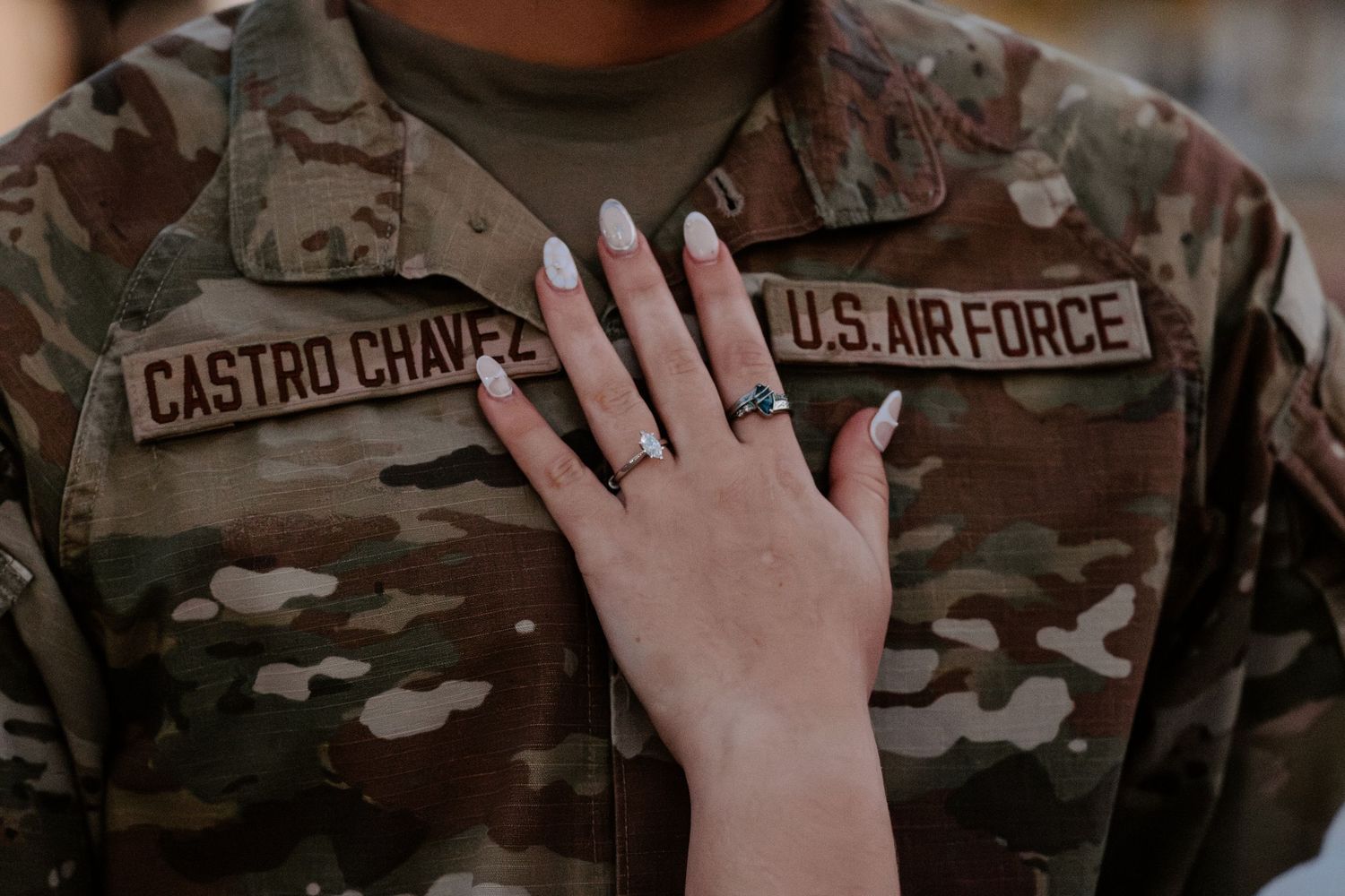 A U.S. Air Force soldier named Castro Chavez wearing camouflage uniform with a hand displaying an engagement ring resting on chest.