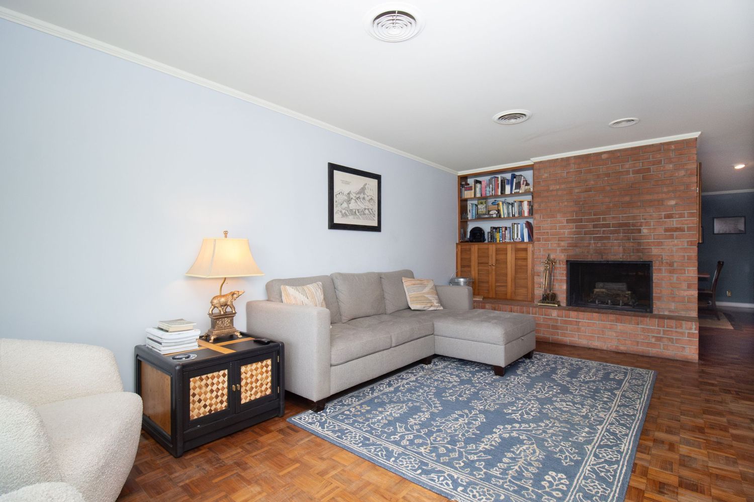 Cozy living room with gray sectional sofa, blue patterned rug, brick fireplace, built-in shelves, and parquet hardwood floors.