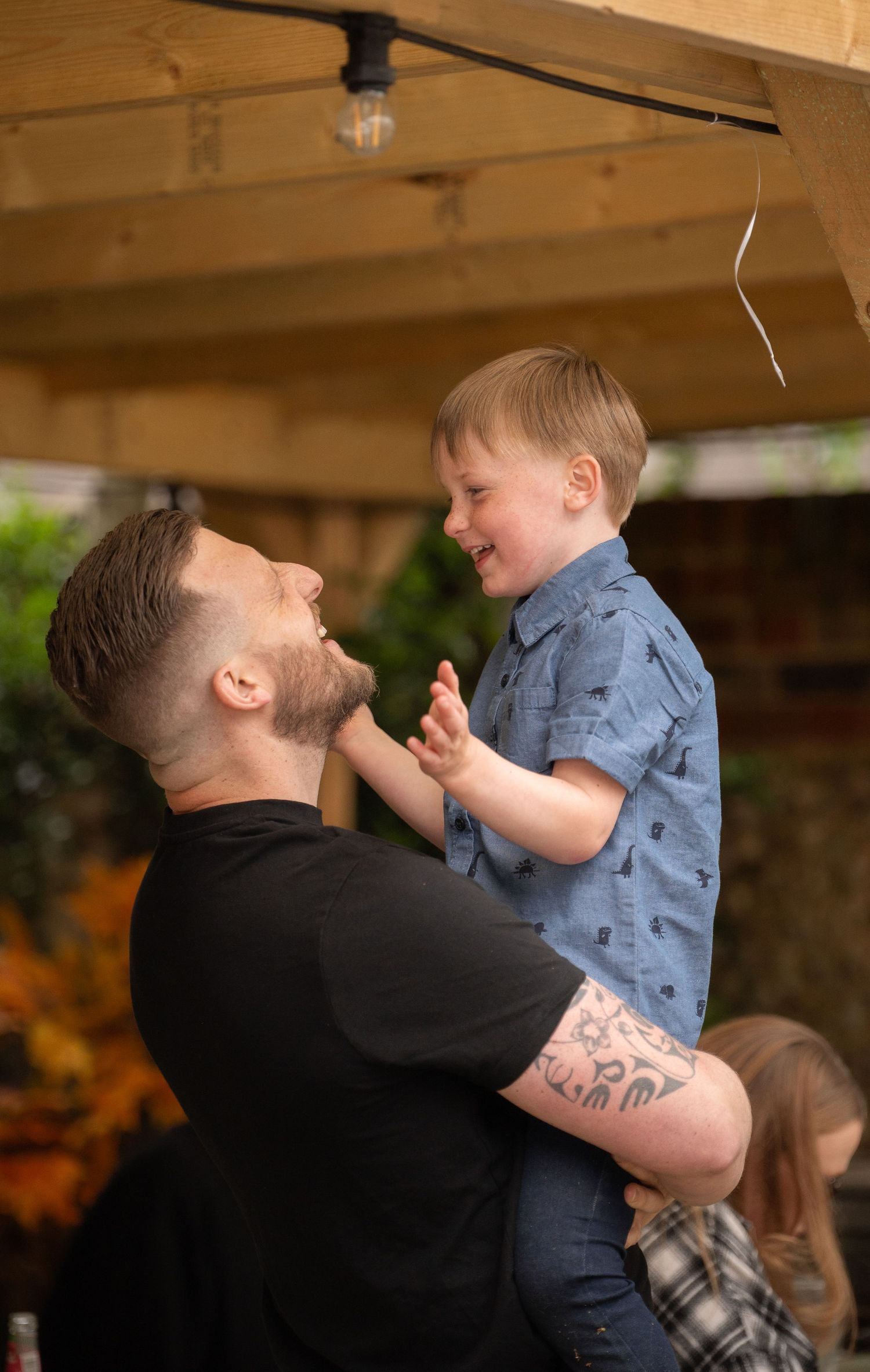 A joyful moment shared between an adult in a black shirt and a small child in a blue patterned button-down shirt.