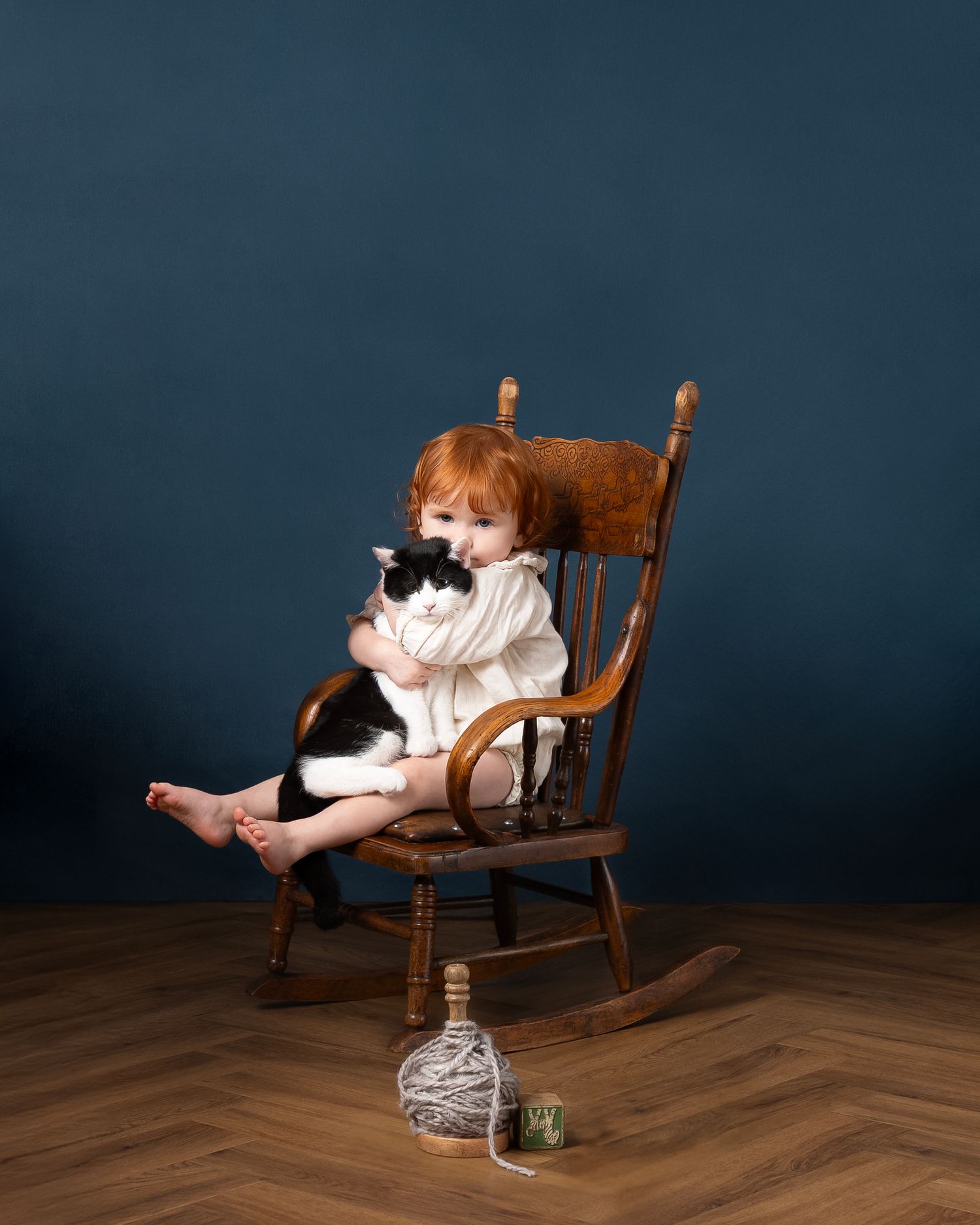 A series of four images showing a child in a white dress playing with yarn while seated in a wooden rocking chair.