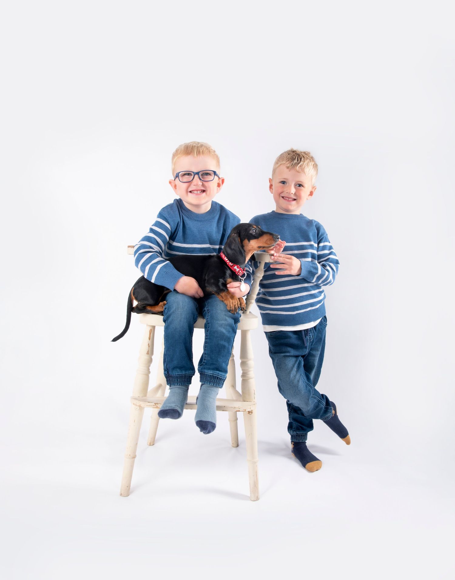 Casual portrait with dachshund puppy and matching blue striped sweaters on white background.