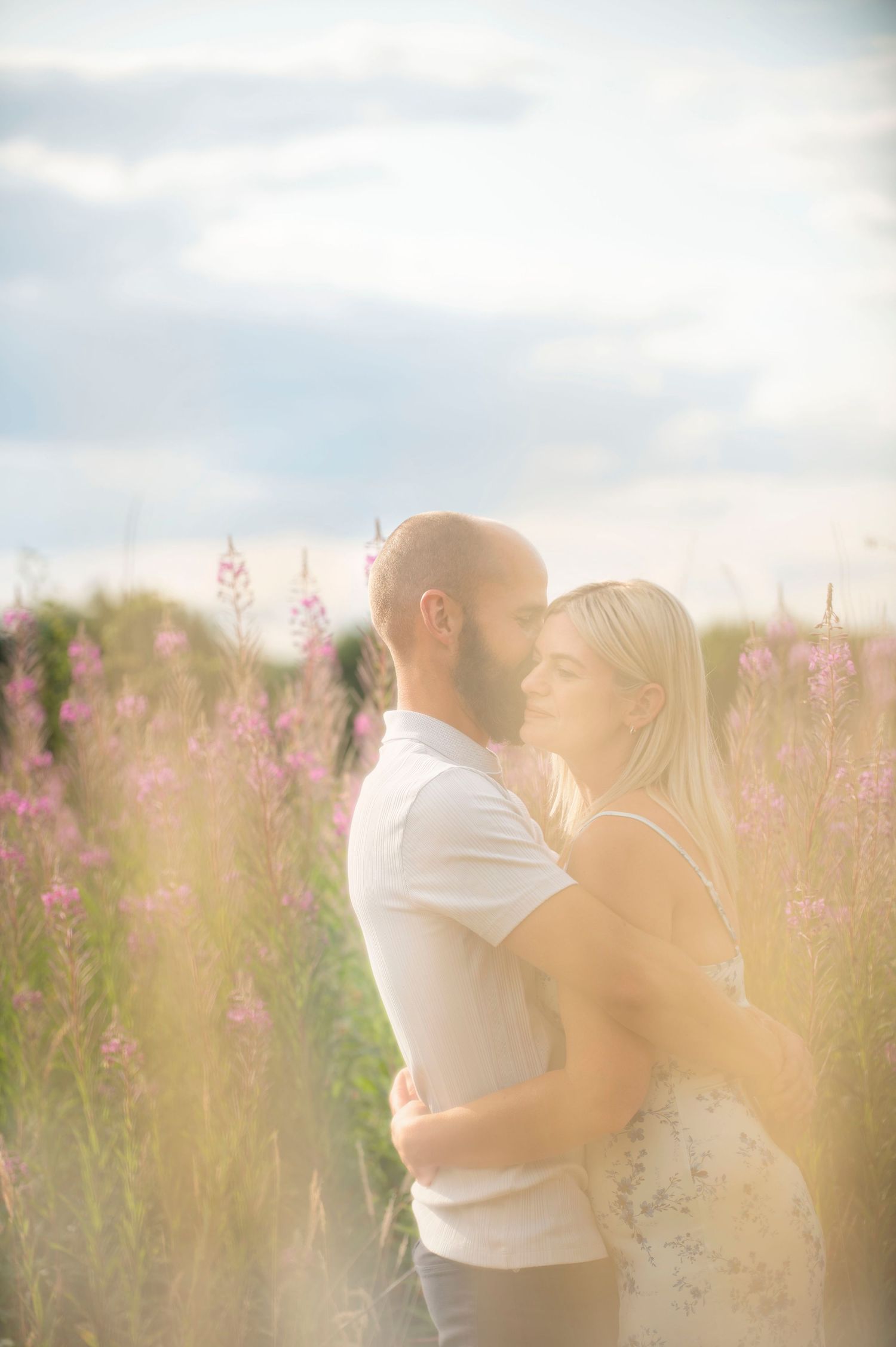 A romantic couple shares an intimate moment in a field of pink wildflowers during sunset.