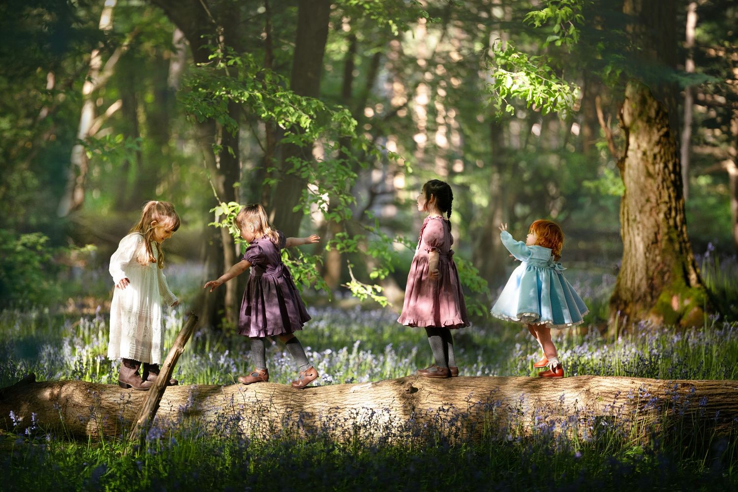 Four girls in vintage dresses playing in an enchanted forest with bluebells and dappled sunlight.