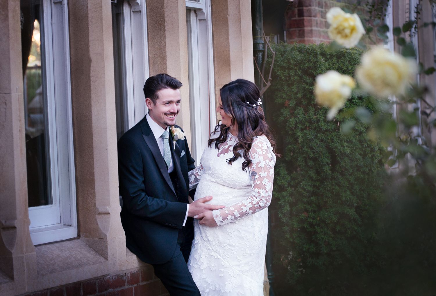 A romantic wedding couple shares a sweet moment outside while yellow roses bloom in the foreground.