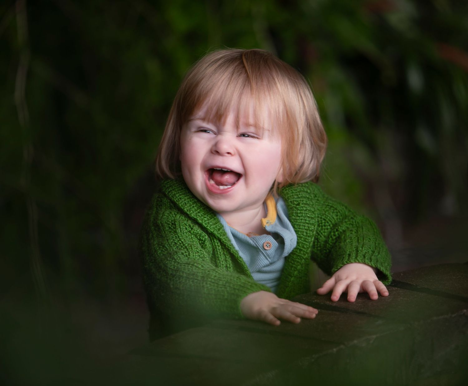 A joyful laugh captured in a portrait wearing a bright green sweater against a dark background.