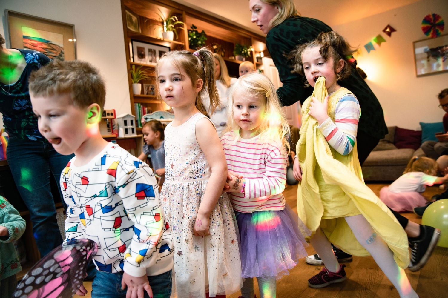 Children dancing and having fun at an indoor party wearing colorful party outfits and dresses.