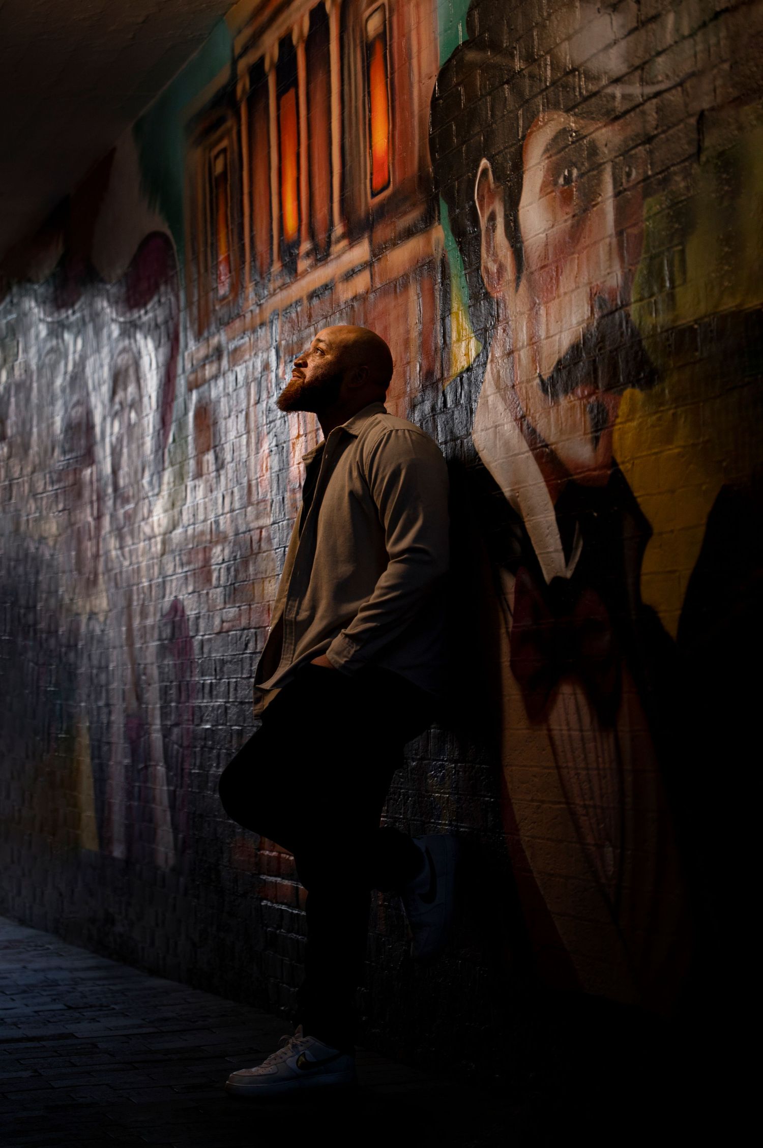 A silhouetted figure stands against a colorful graffiti wall in a moody urban alleyway illuminated by warm lighting in St Albans.