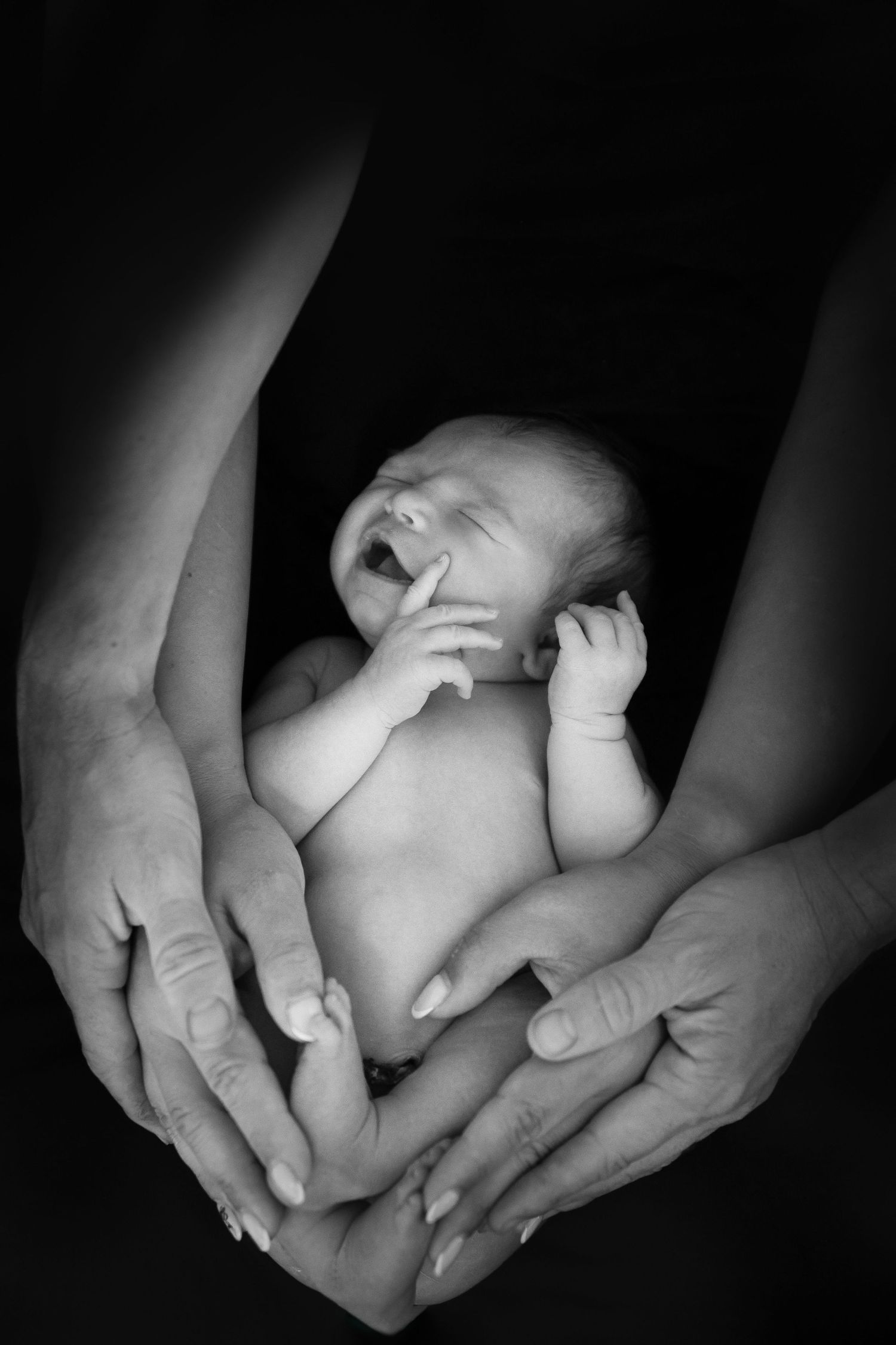 A newborn baby sleeps peacefully in gentle hands, captured in black and white.