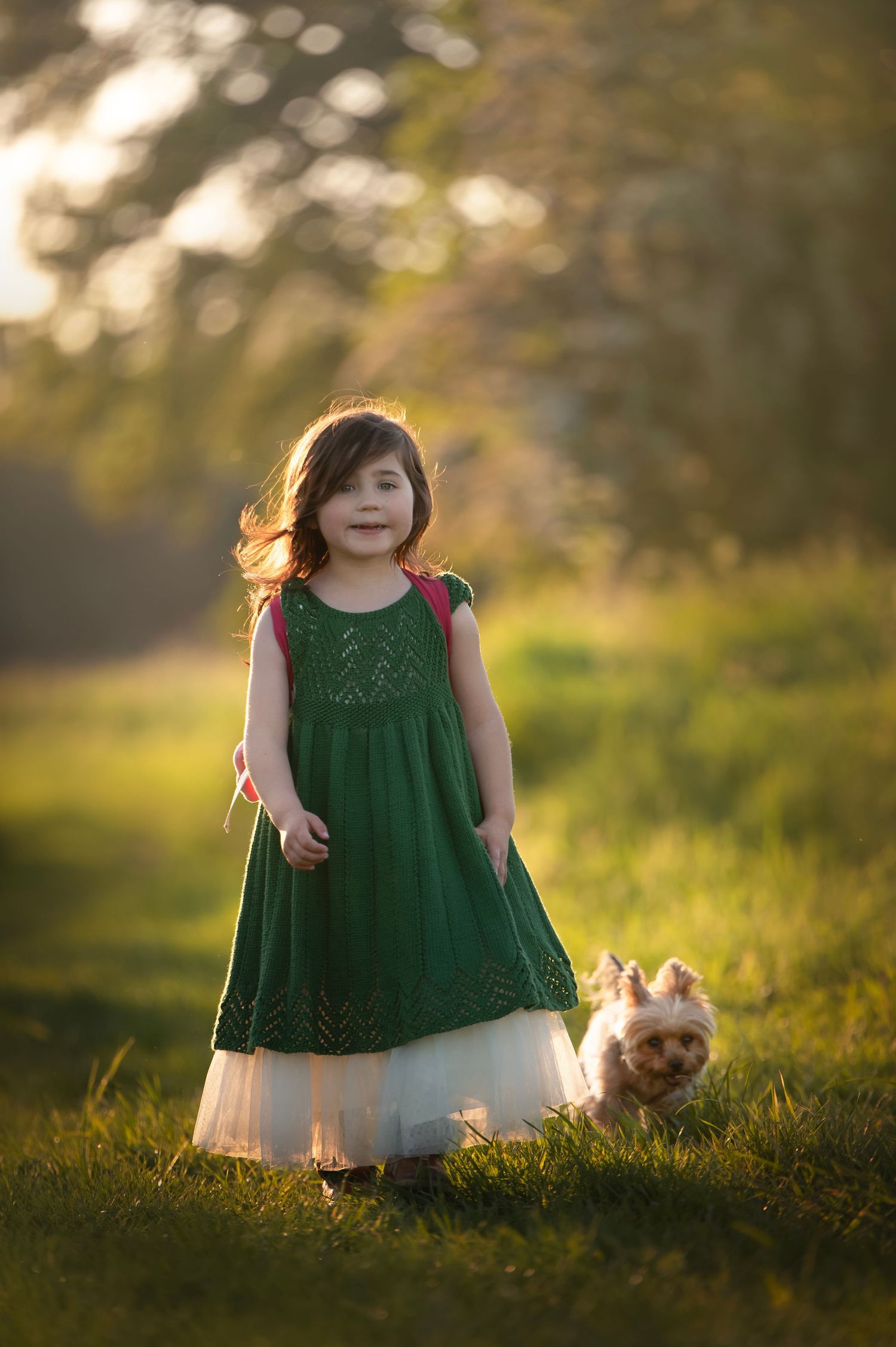 Emerald green dress against golden sunset light in grassy field.