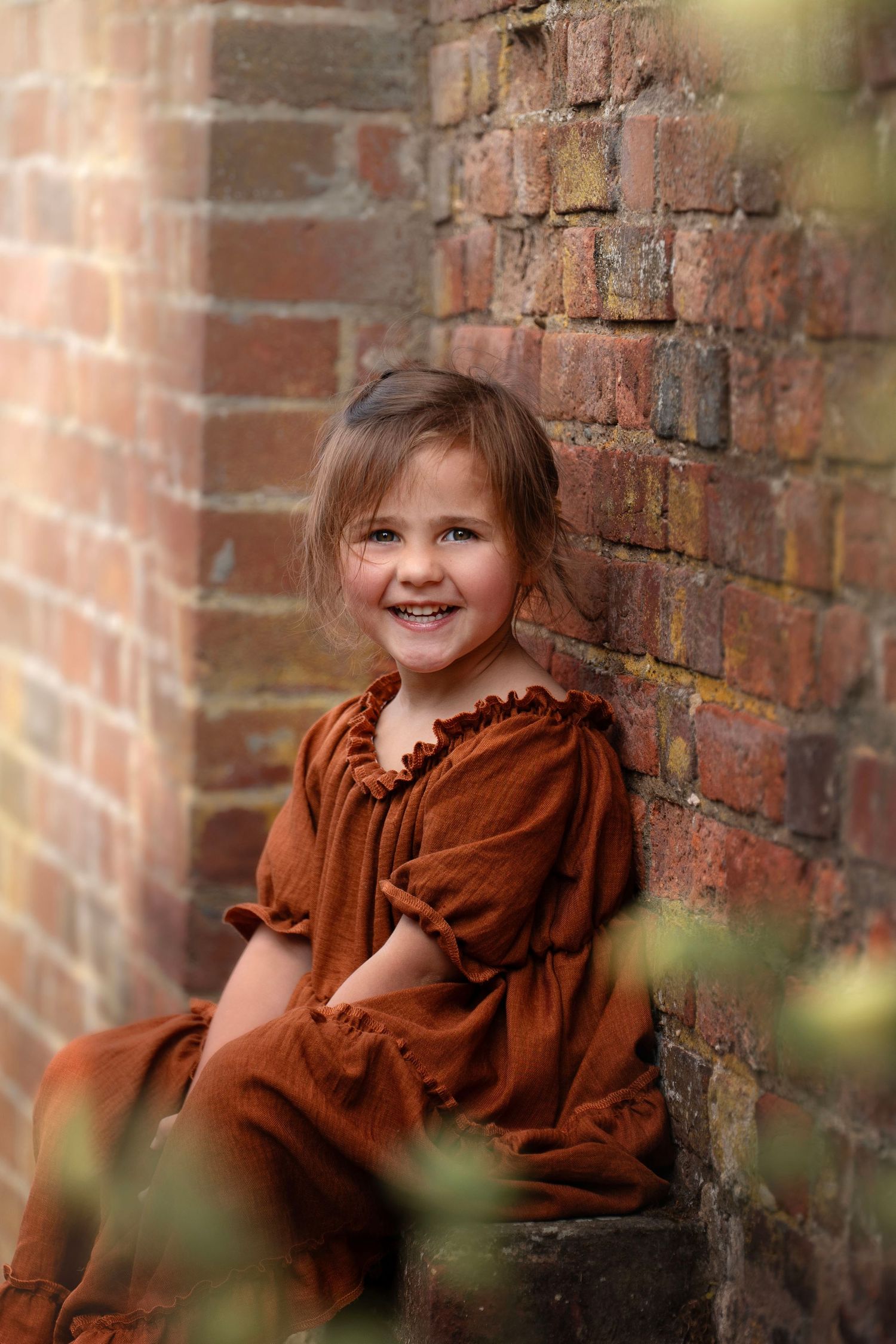 Vintage-style portrait against rustic brick wall showing brown ruffled dress.