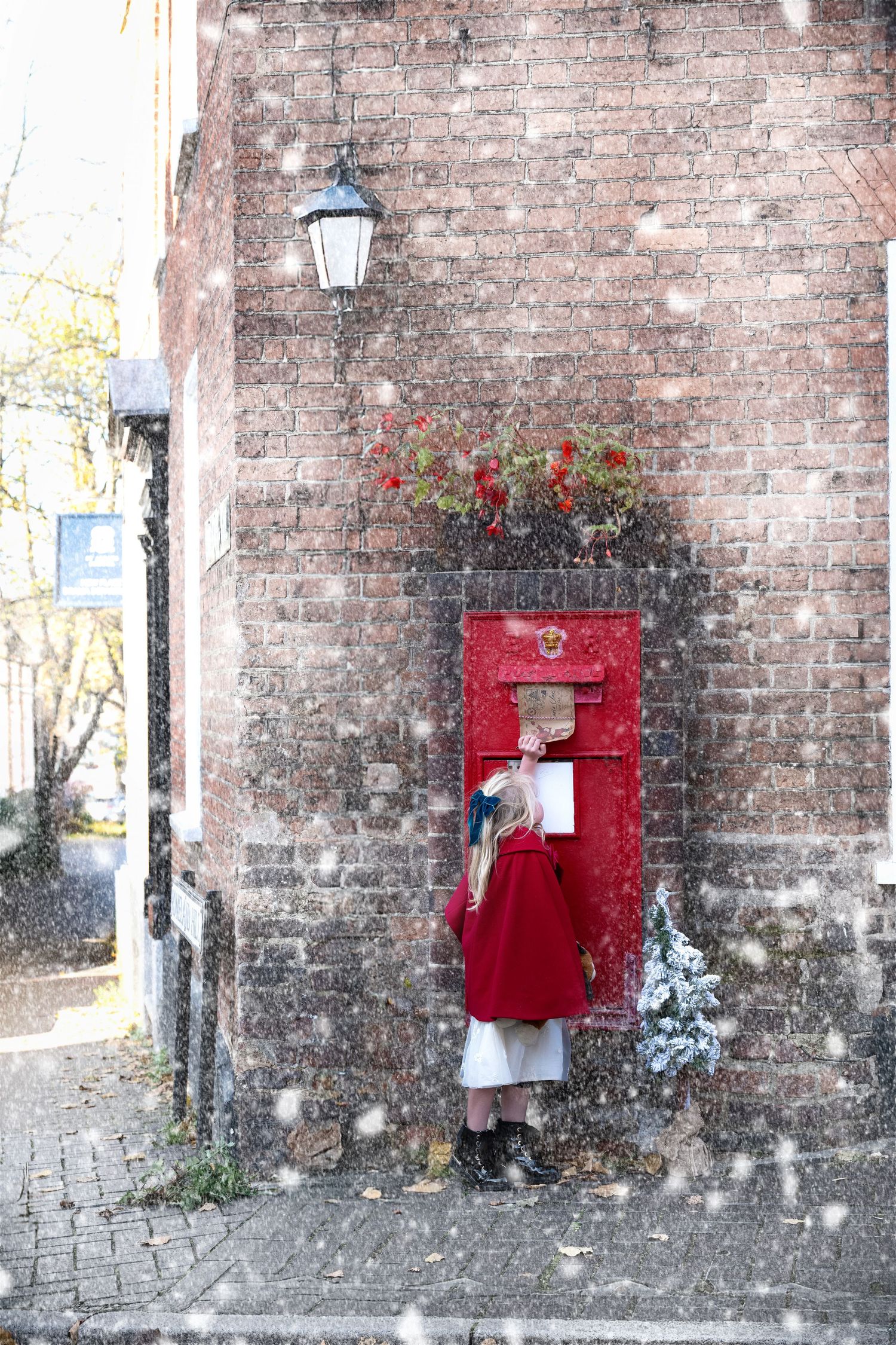 A series of four red mailboxes mounted on a weathered brick wall with a vintage lantern and flowers nearby.