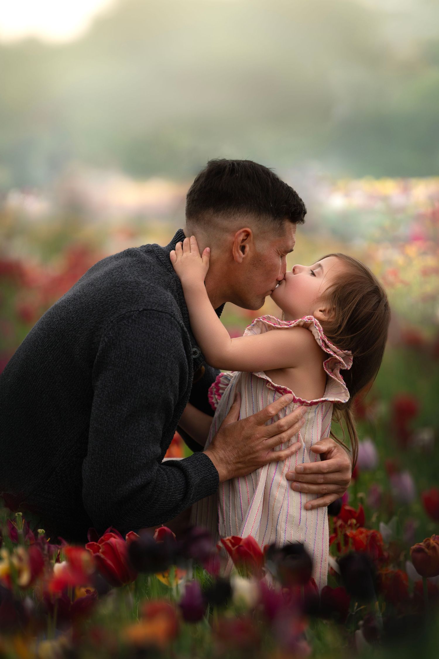A tender moment shared between parent and child among blooming red tulip flowers at sunset.