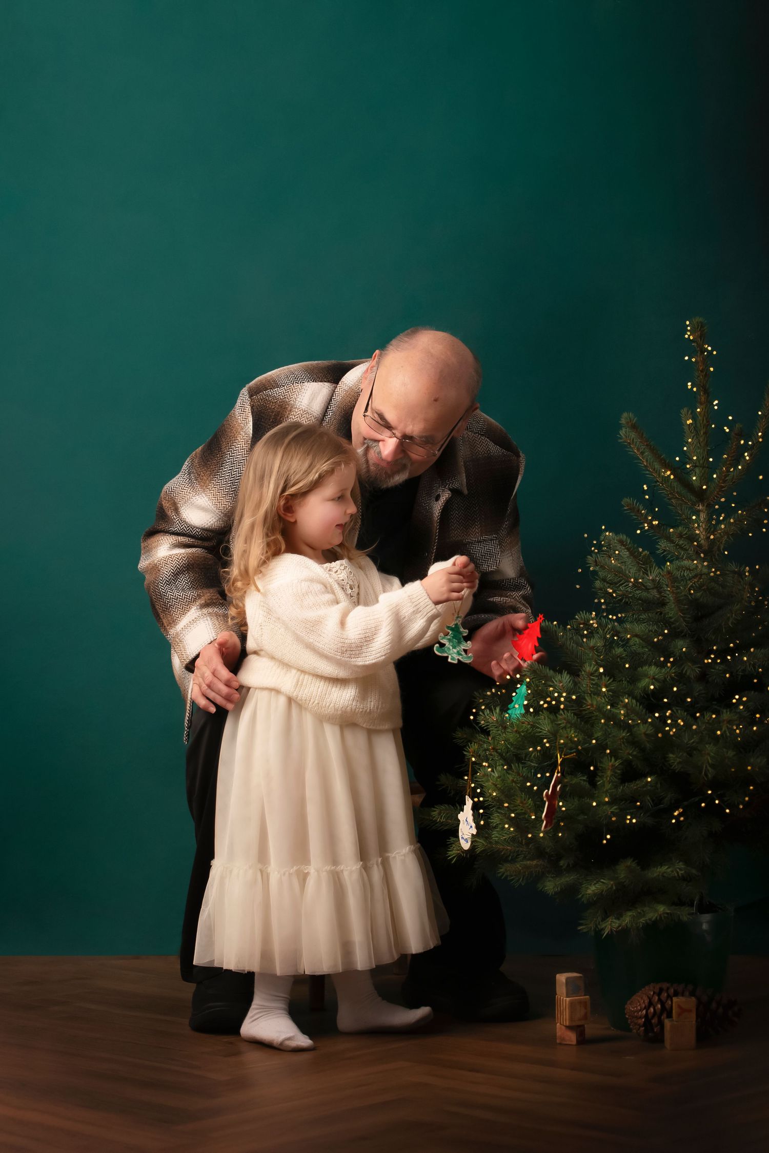 A small child in a white dress is held and comforted near a Christmas tree in a series of heartwarming photos.