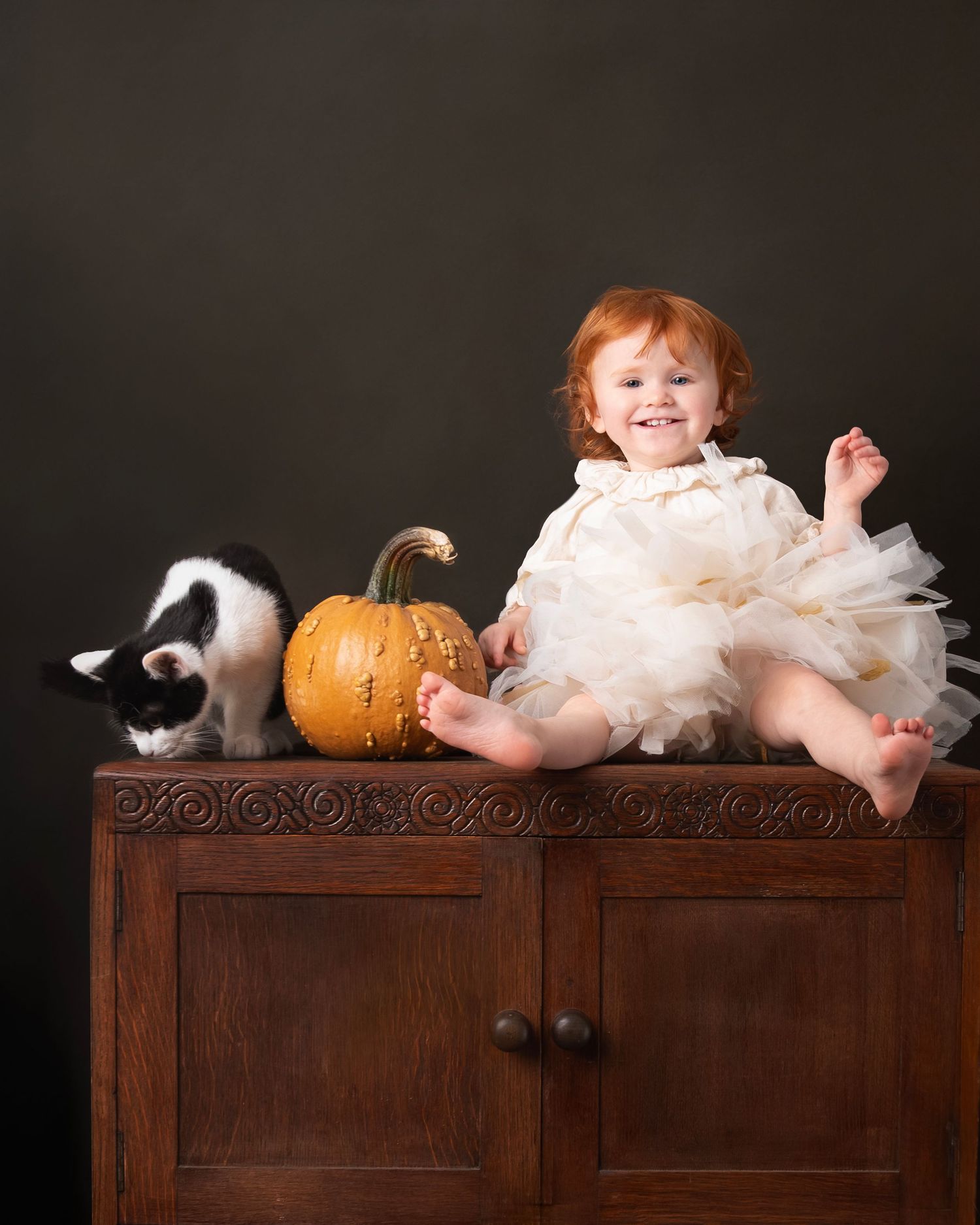A series of five photos showing a baby in a white dress lying on an antique wooden dresser with a pumpkin decoration.