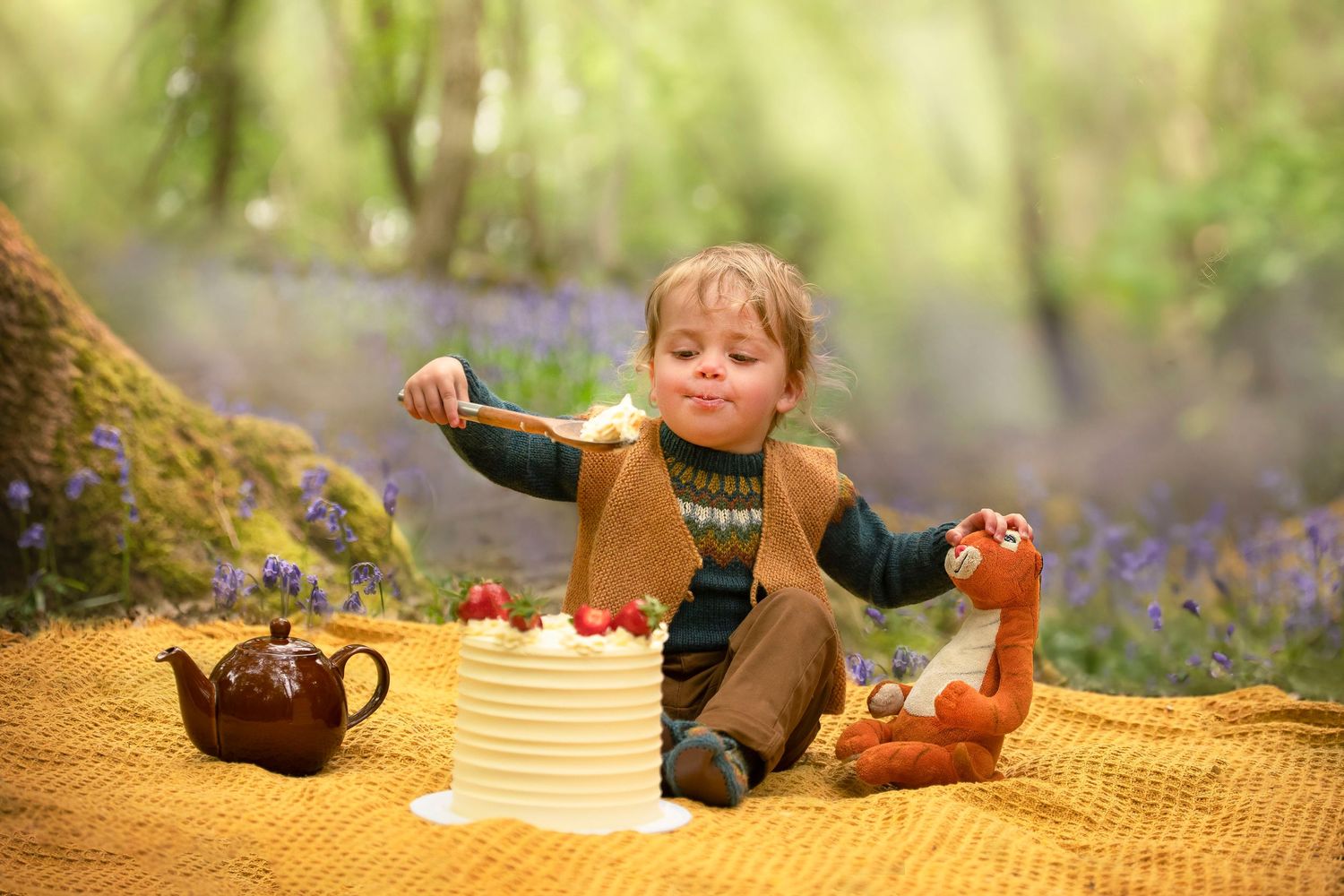 Young boy reaching for strawberries on a white cake during an outdoor woodland birthday tea party photoshoot.