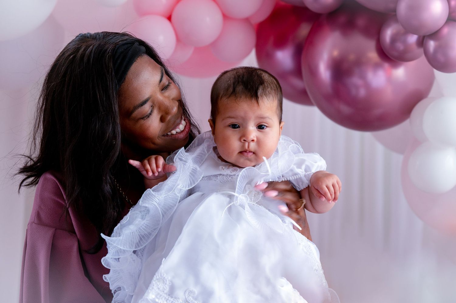 Two people share a joyful moment against a pink balloon backdrop in celebration attire.