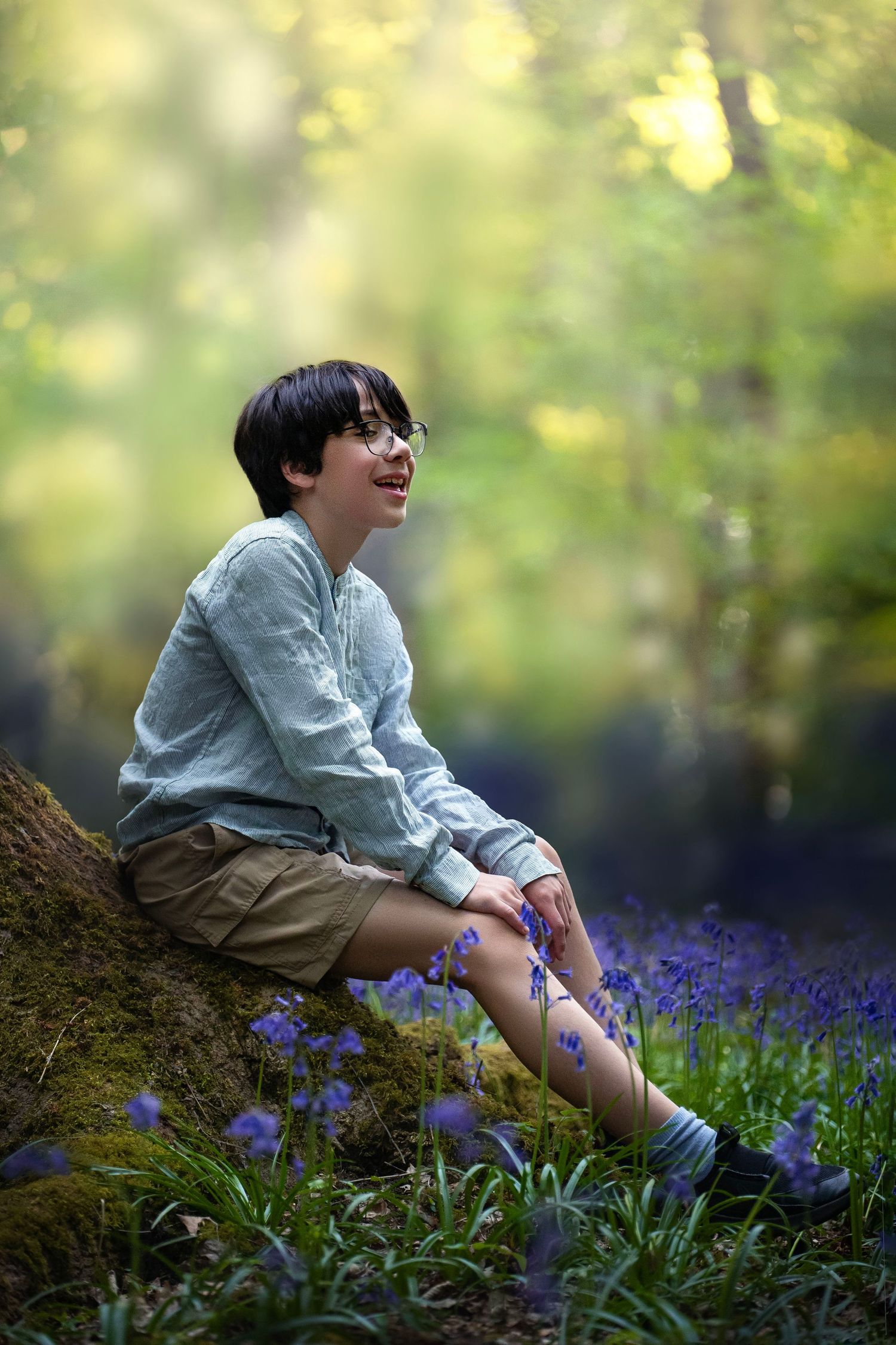A person sits on a mossy log surrounded by blooming purple wildflowers in a dreamy forest setting.