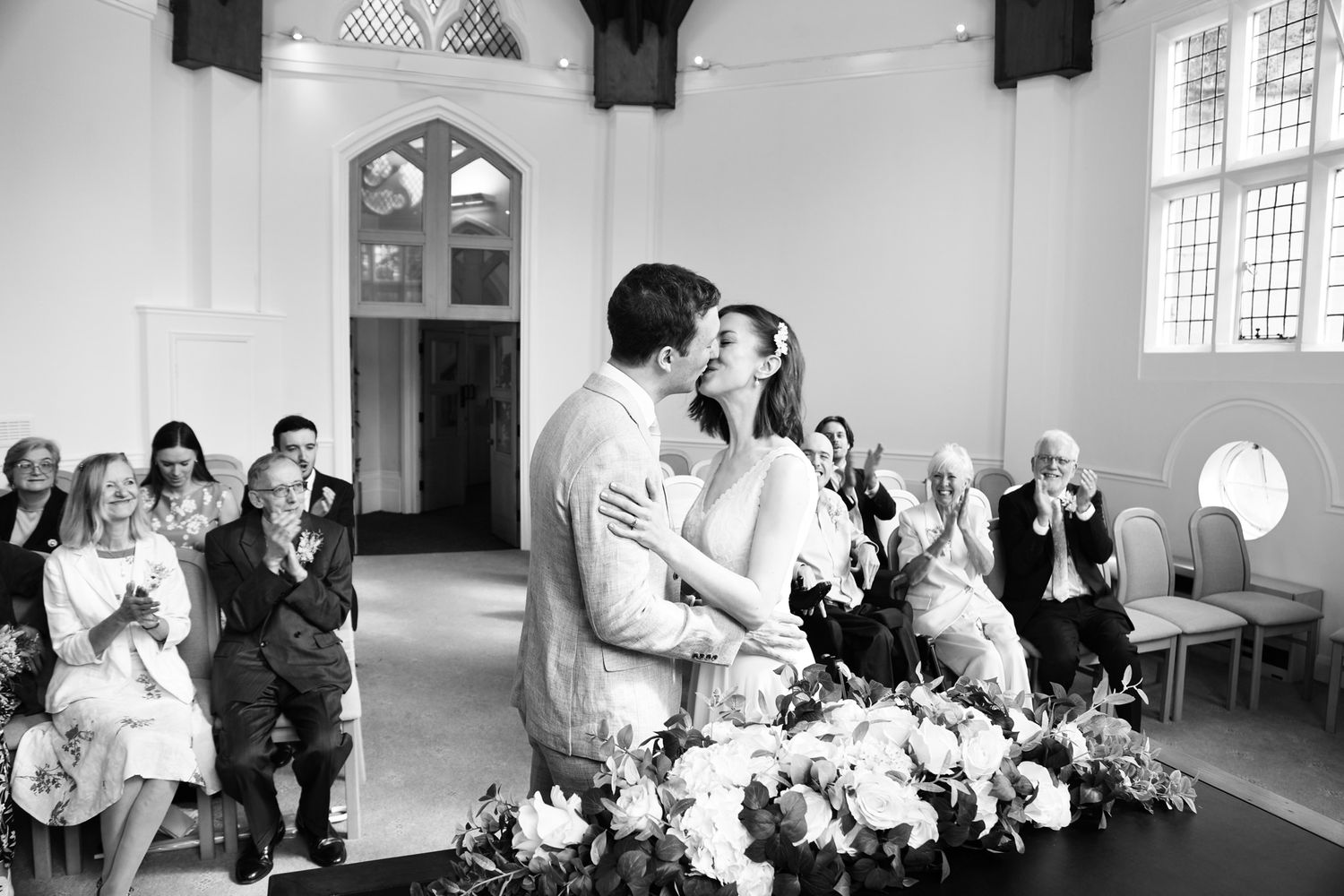 A series of black and white wedding photographs arranged in a horizontal strip showing intimate moments at a church ceremony.