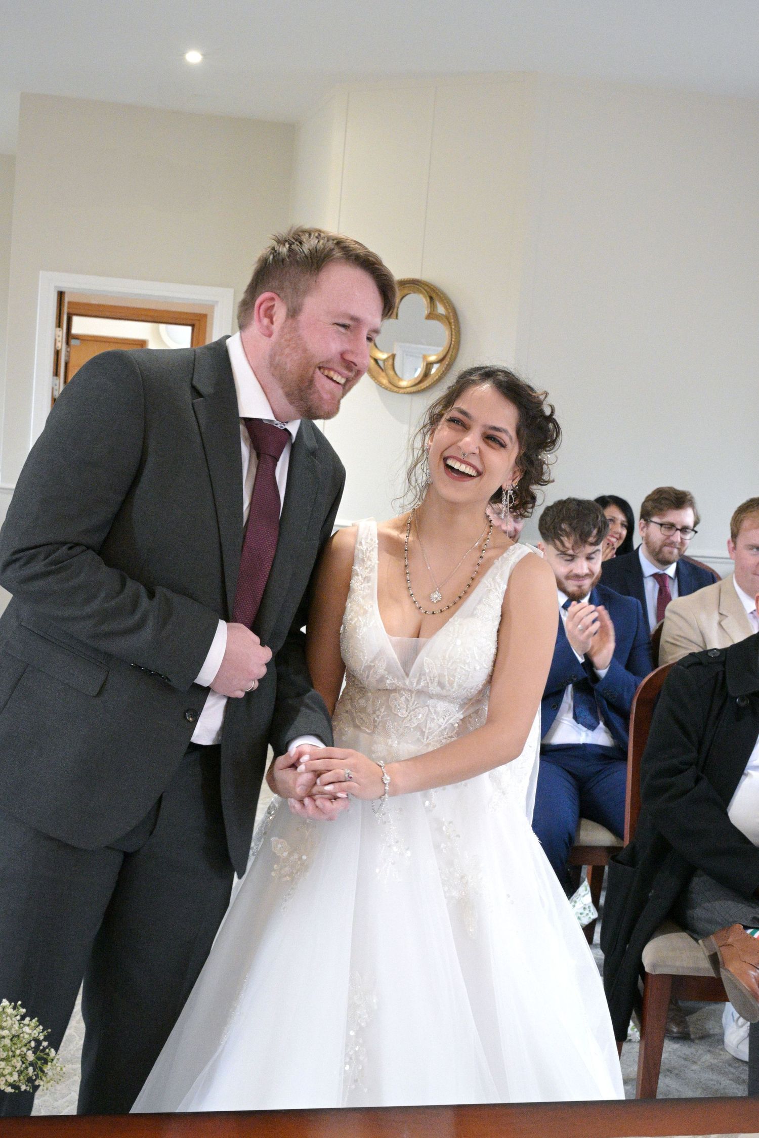 A joyful bride and groom laugh together during their wedding ceremony while guests applaud in the background.