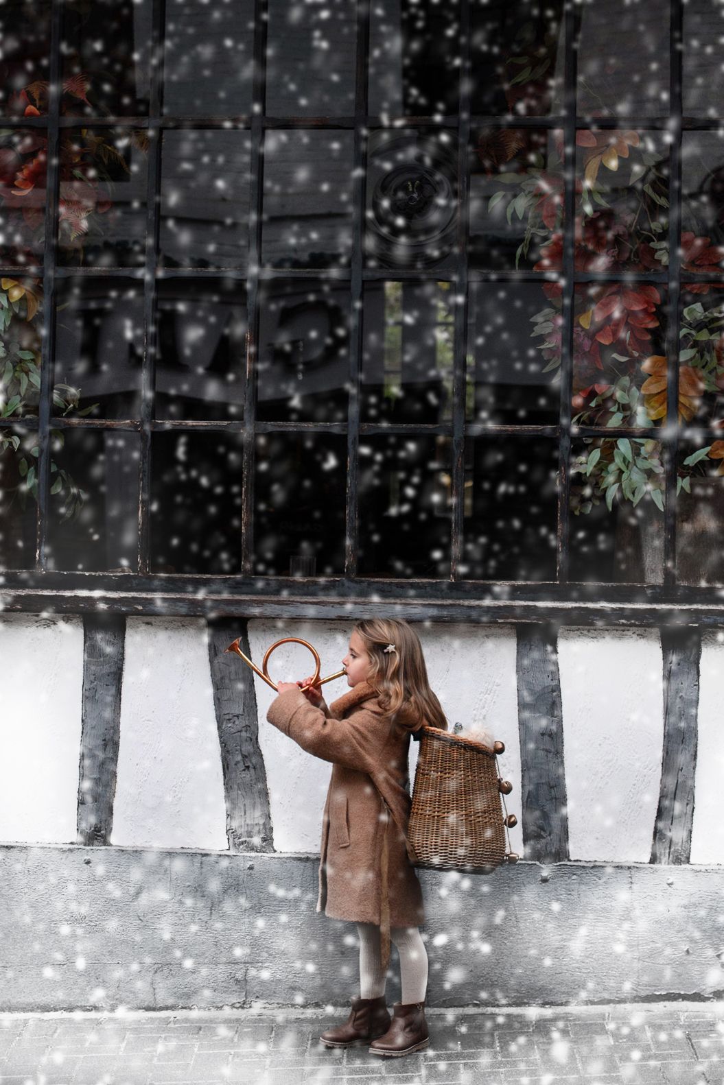 A child in a brown coat stands in a snowy winter scene with falling snowflakes against a dark background.