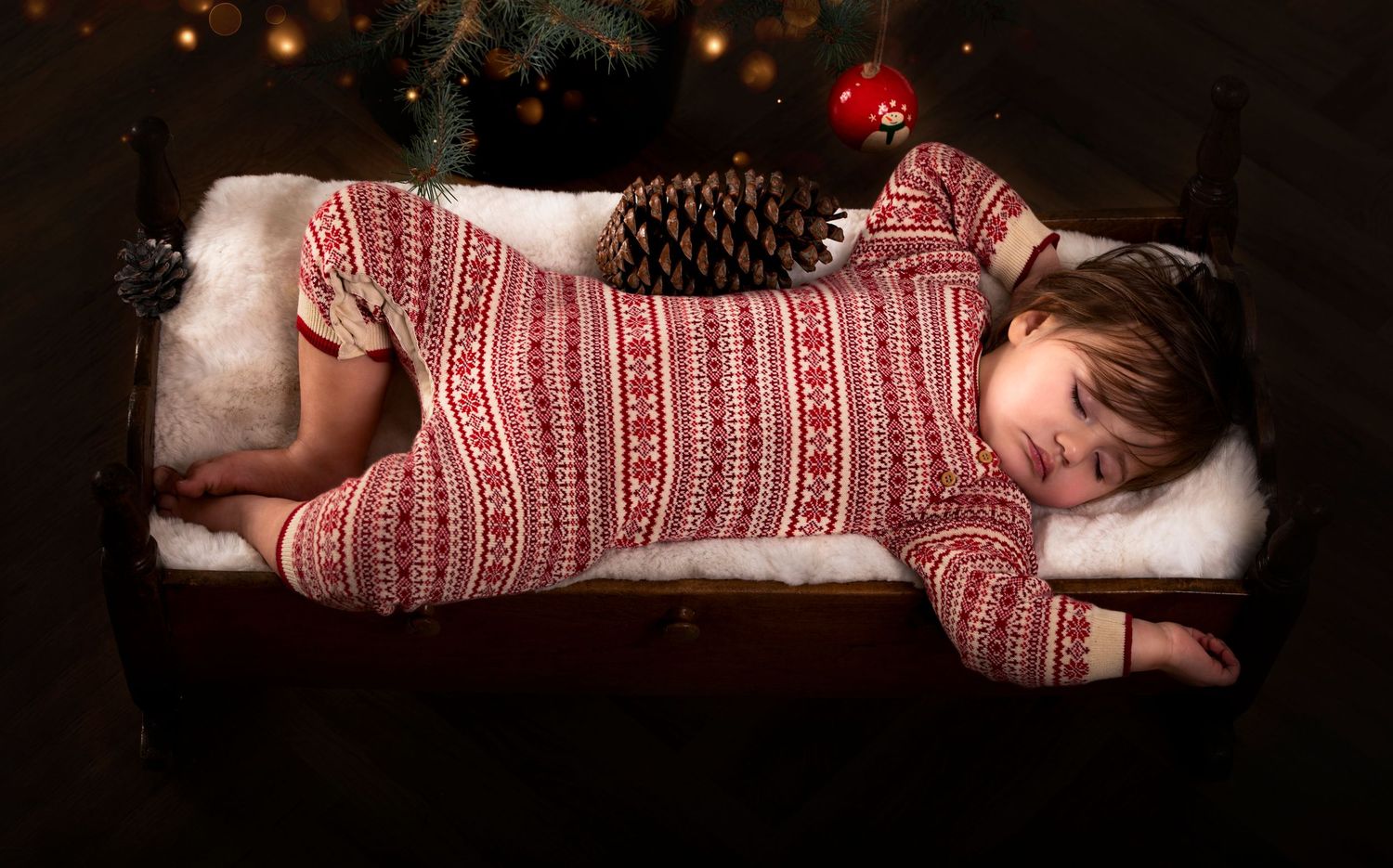 Sleeping child in red and white patterned holiday sweater resting near Christmas lights.