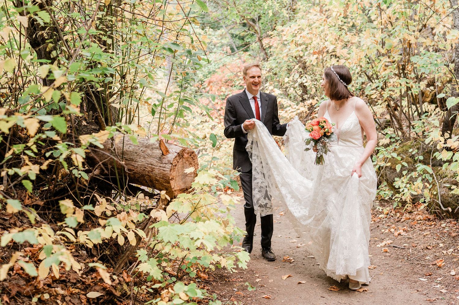 Groom holds brides dress as they walk through a lush forest path surrounded by autumn foliage in Leavenworth, WA.