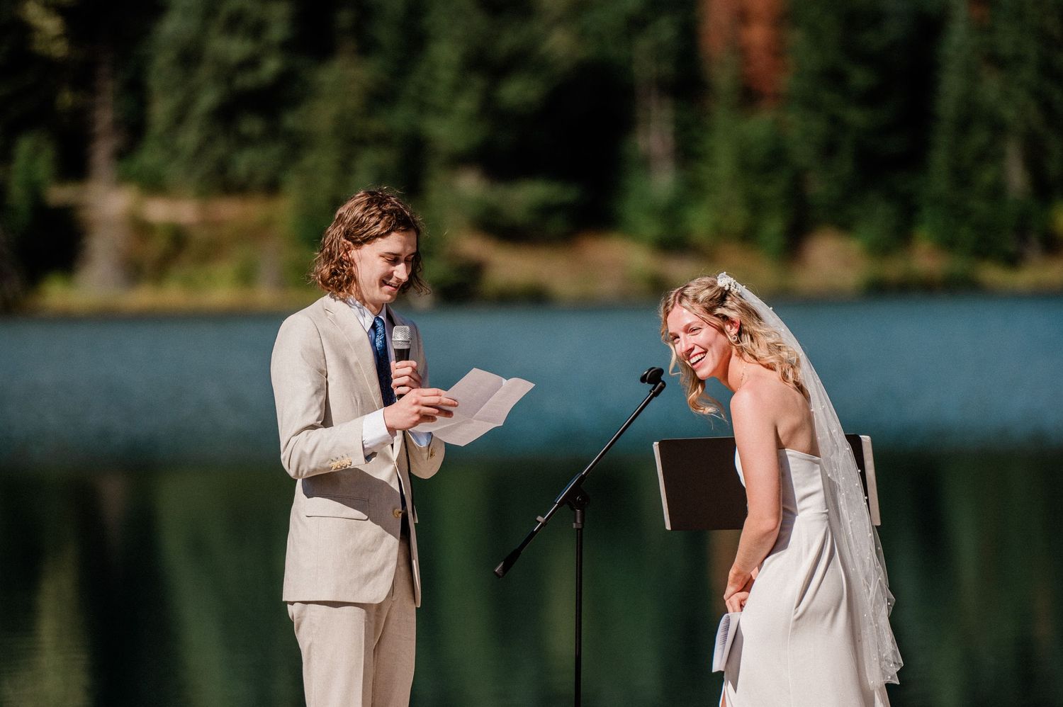 Bride and groom laughing during their lakeside ceremony at sunset.