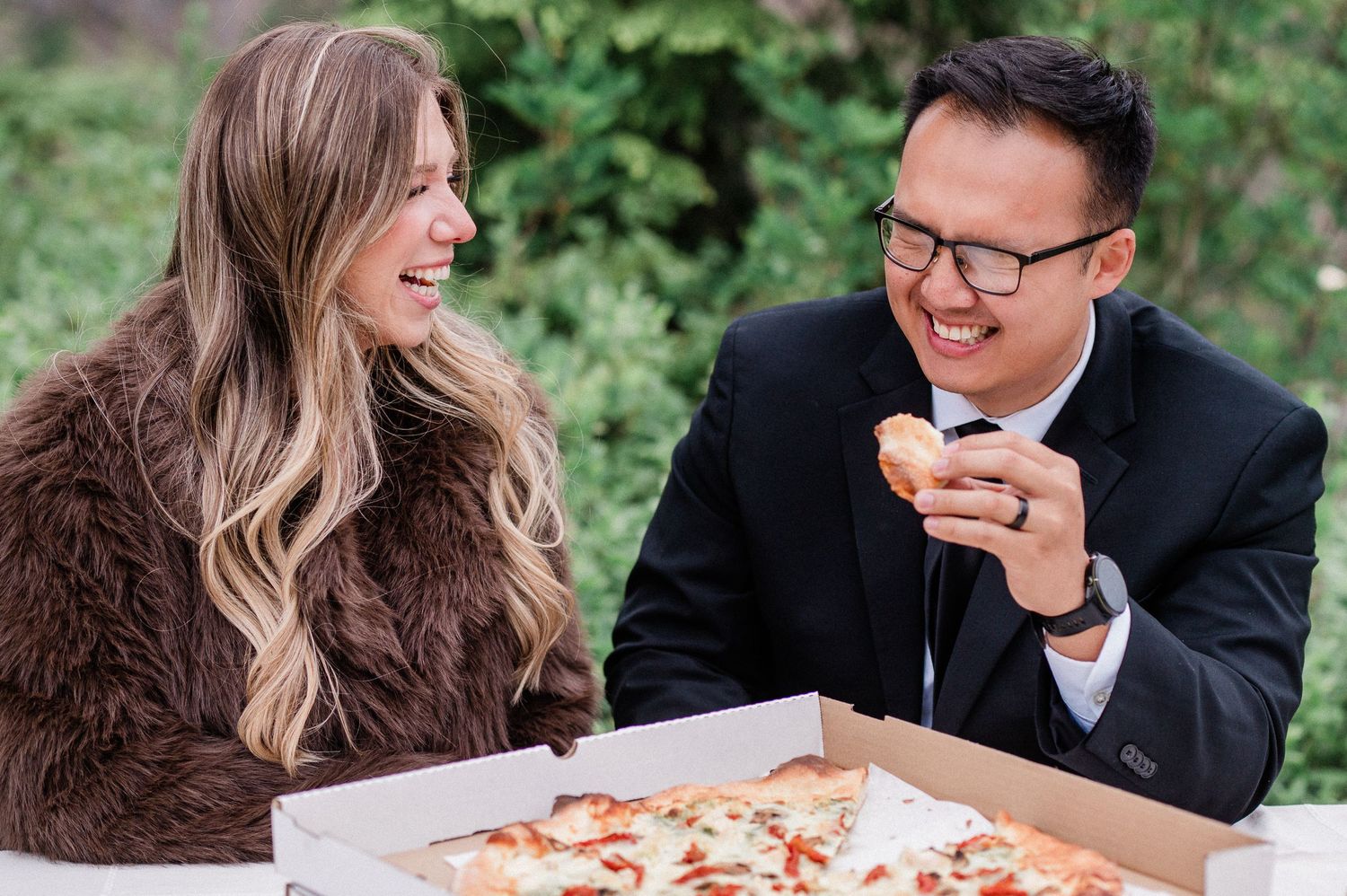 bride and groom laugh while eating pizza