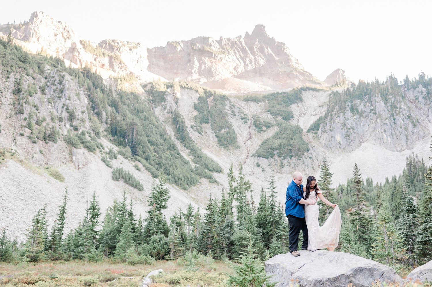 bride and groom on top of a rock with a rocky mountain behind them during their Mt. Rainier elopement.