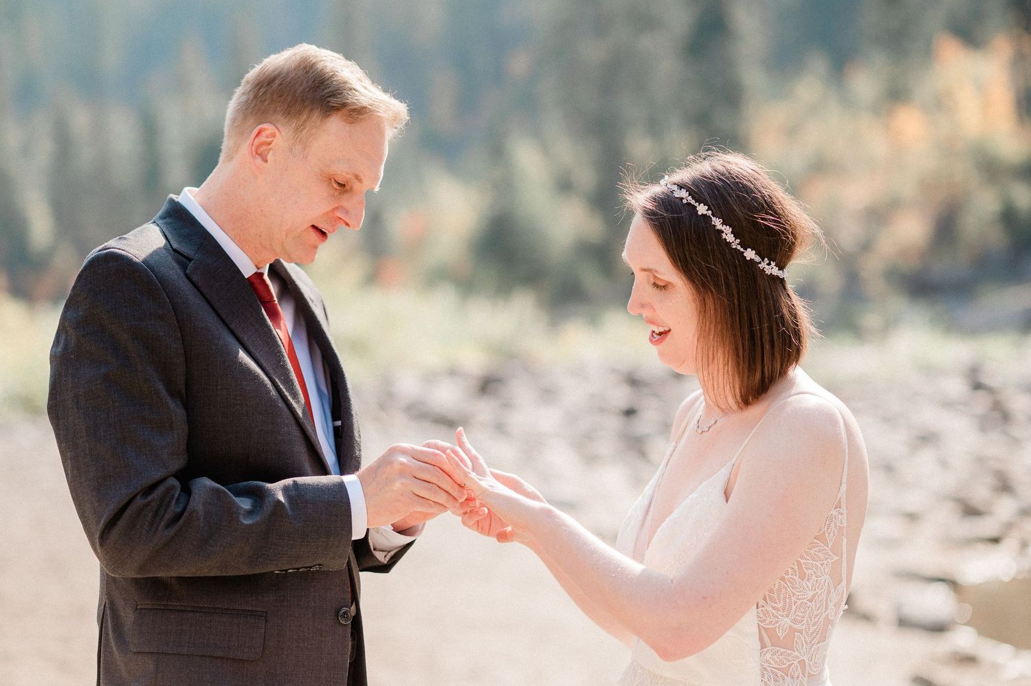 A couple exchanges rings during an outdoor wedding ceremony in a scenic mountain setting. Photo by Pine + Vow