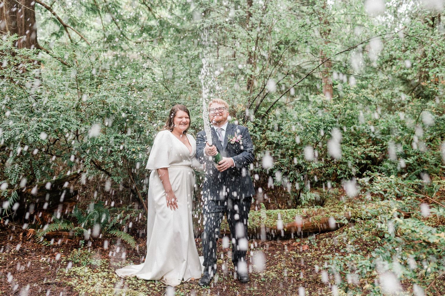 Bride and groom spraying champagne in a forest during their elopement.