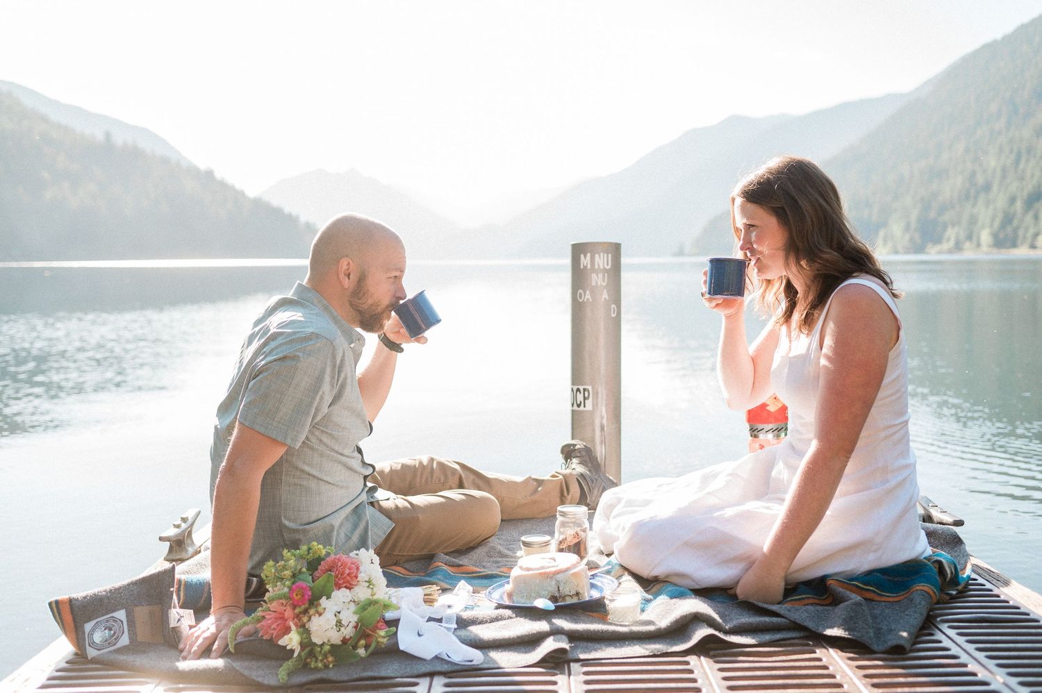 A newlywed couple enjoys a romantic breakfast picnic on a dock overlooking Lake Crescent in Olympic National Park.