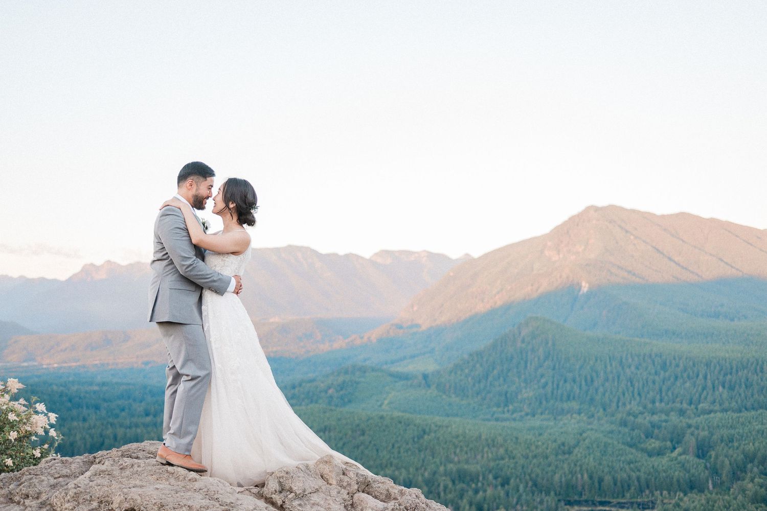 bride and groom embrace on top of a mountain with the sun setting creating the mountains behind them to glow pink.