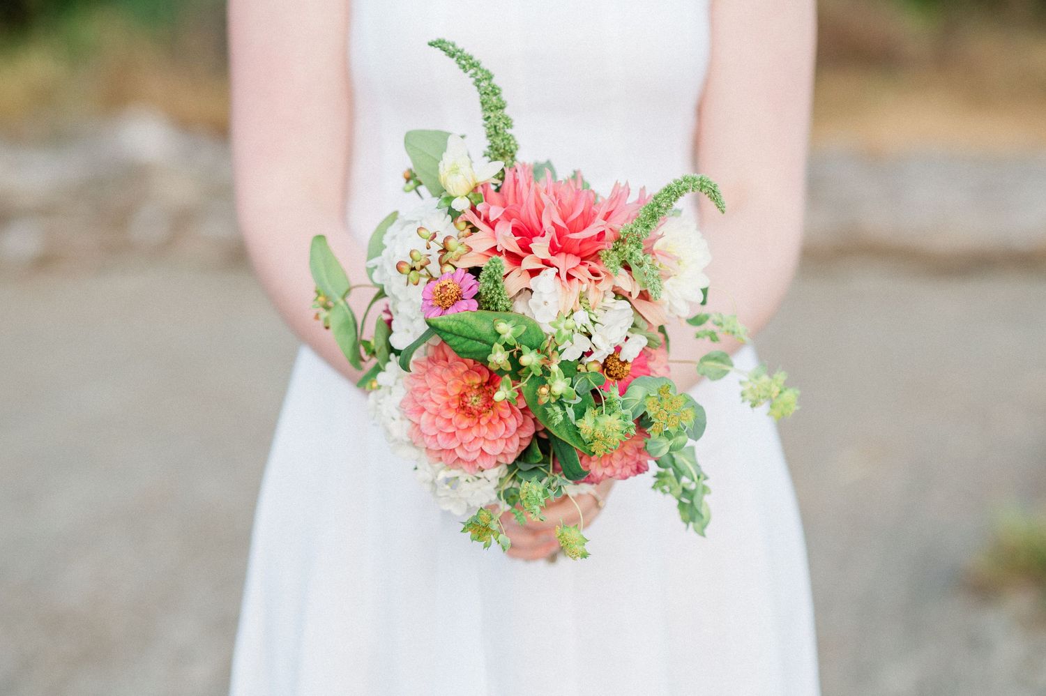 A delicate coral and pink floral wedding bouquet with white accents held against a white dress.