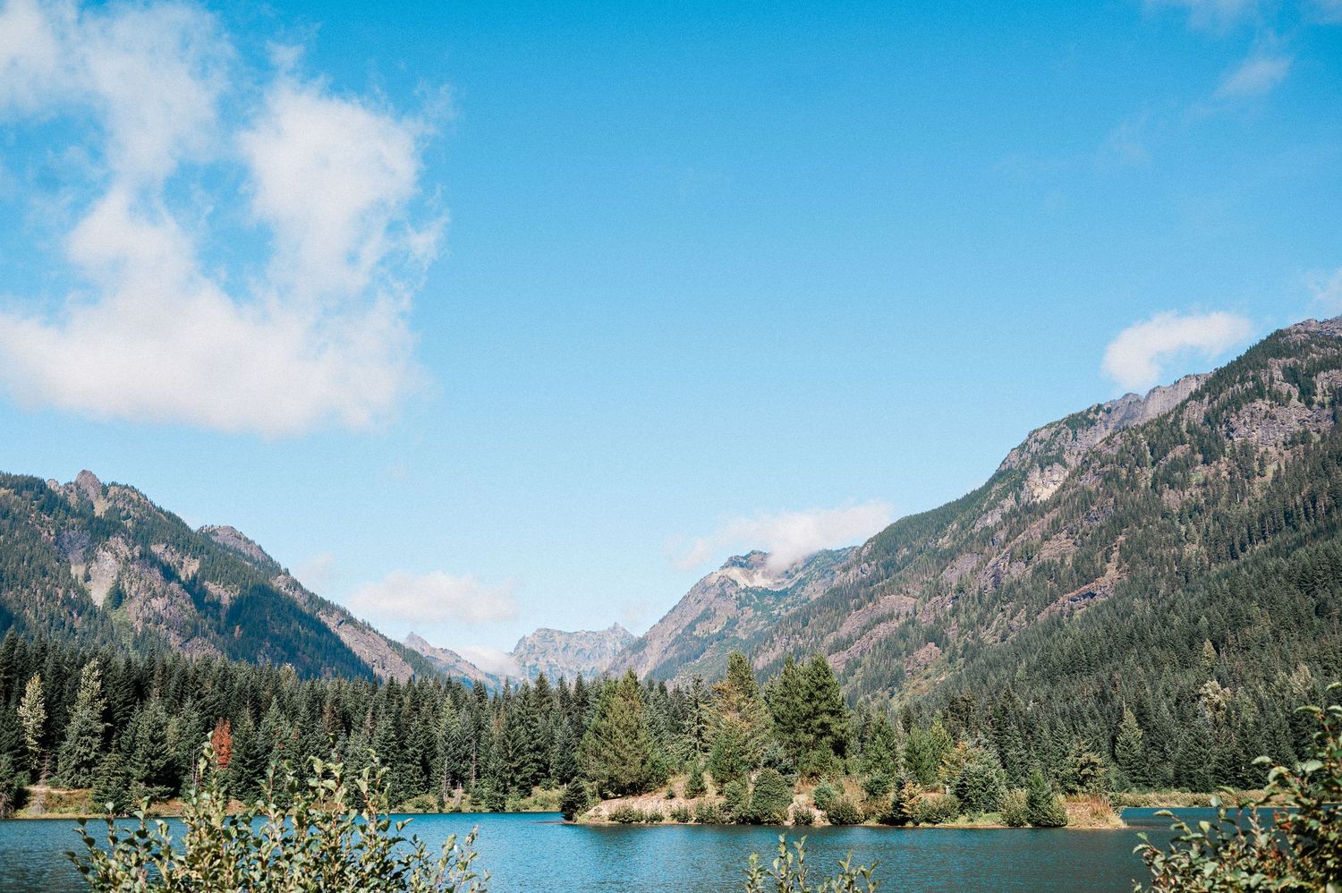 Scenic mountain lake surrounded by evergreen forests and snow-capped peaks under blue skies in a pristine wilderness at Gold Creek Pond.