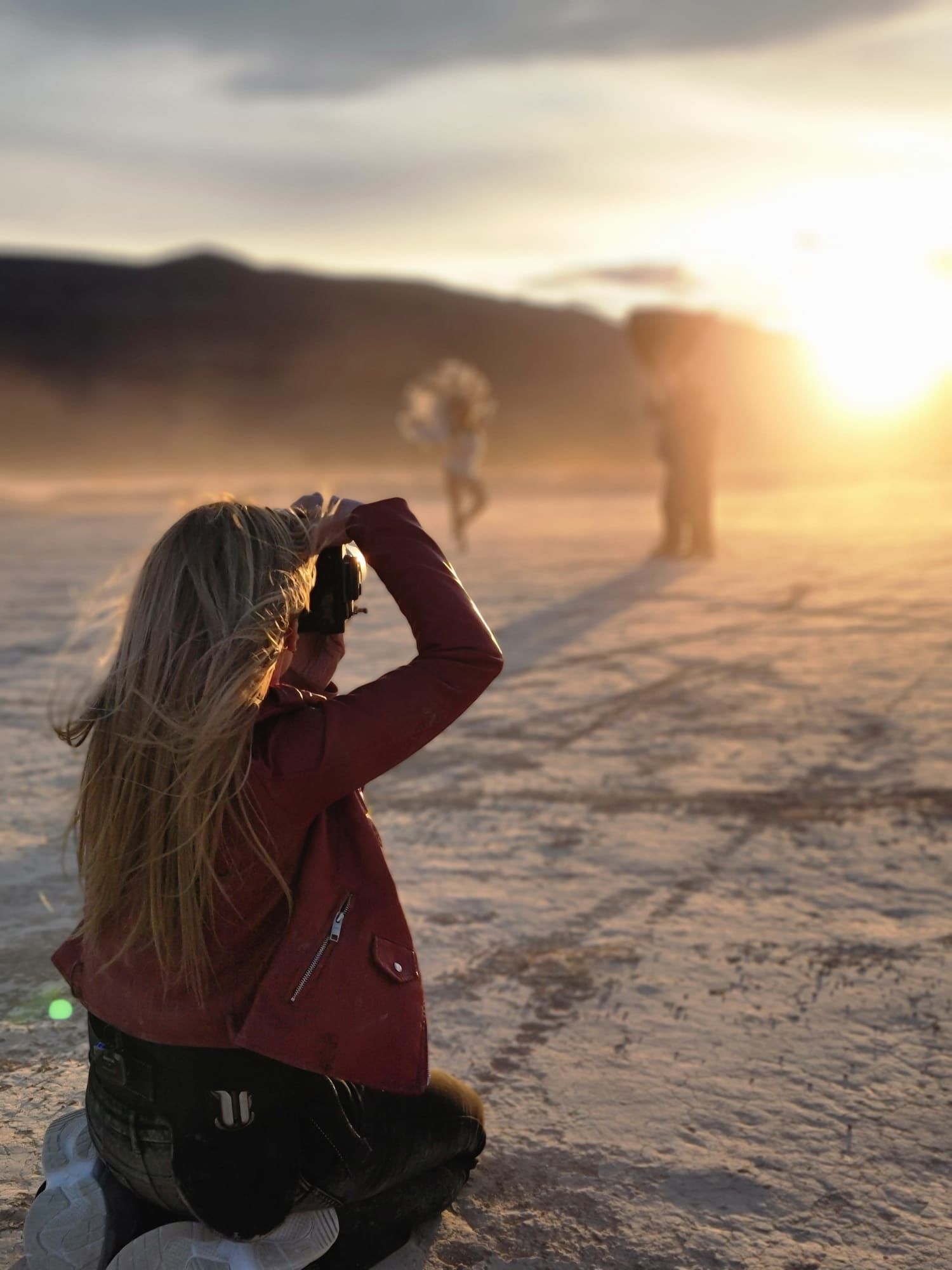 Person in red jacket photographing during golden sunset on snowy terrain.