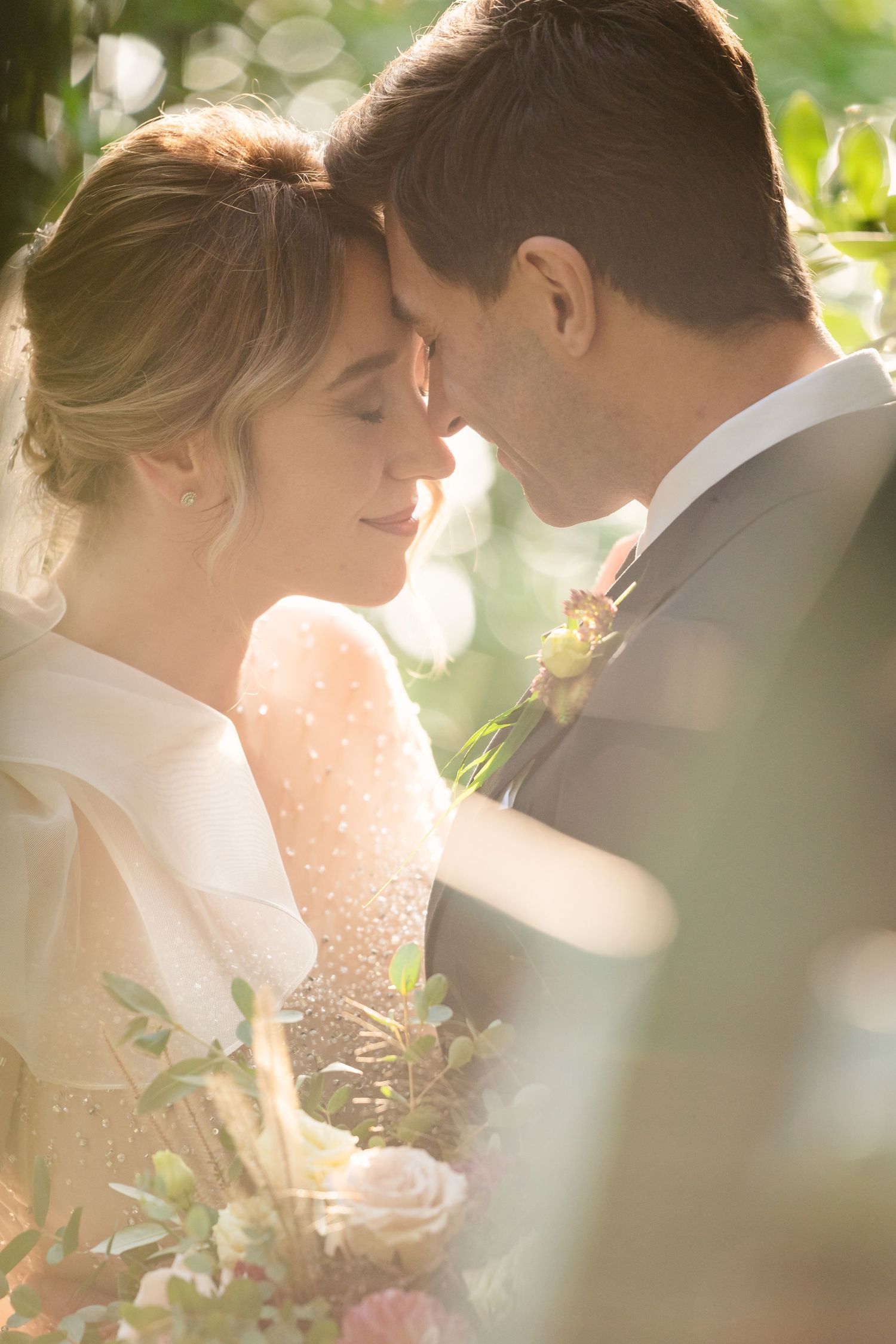 Romantic sunlit wedding moment captured through green foliage.
