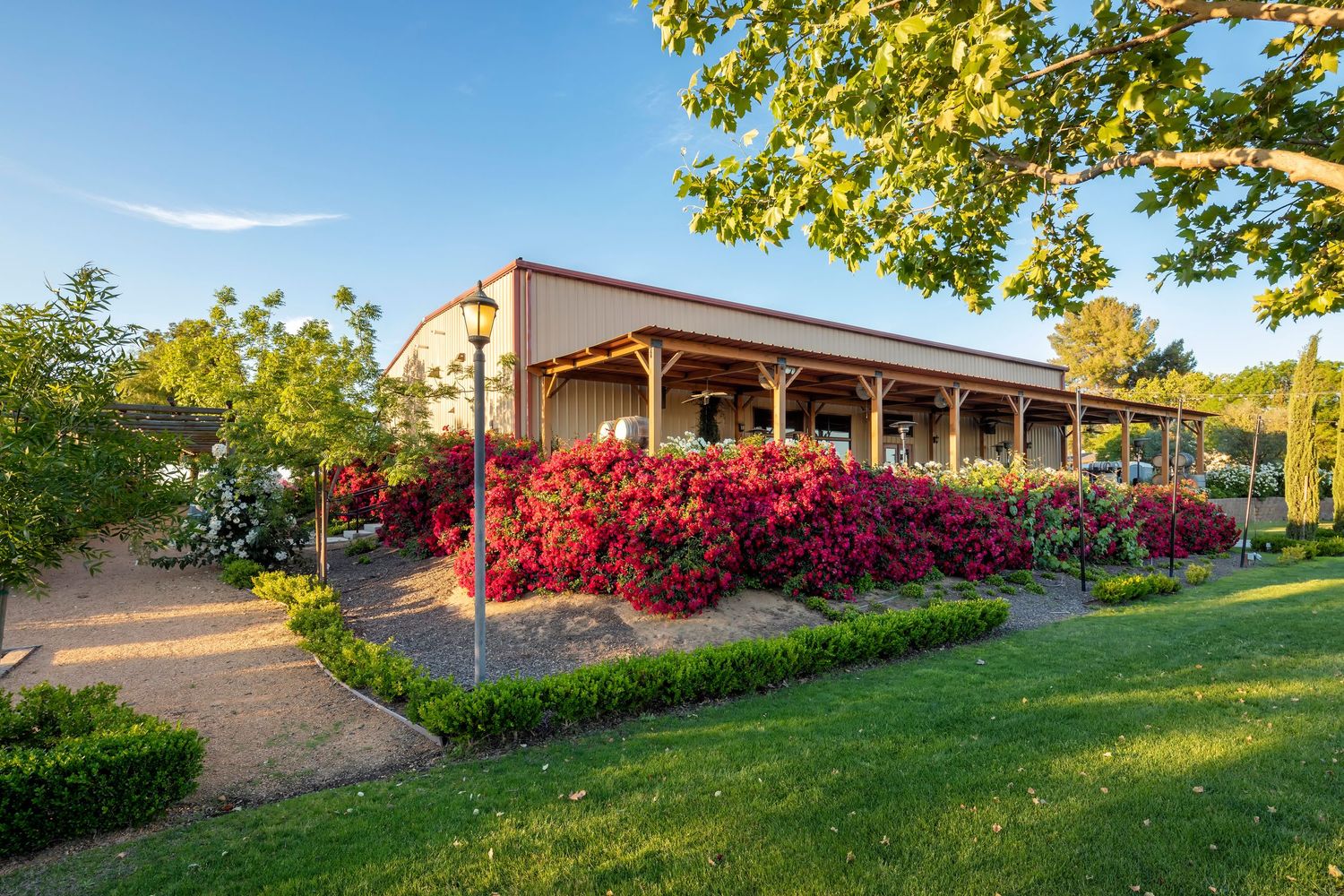 A panoramic view of a modern building exterior with lush landscaping and vibrant red azalea bushes in bloom.