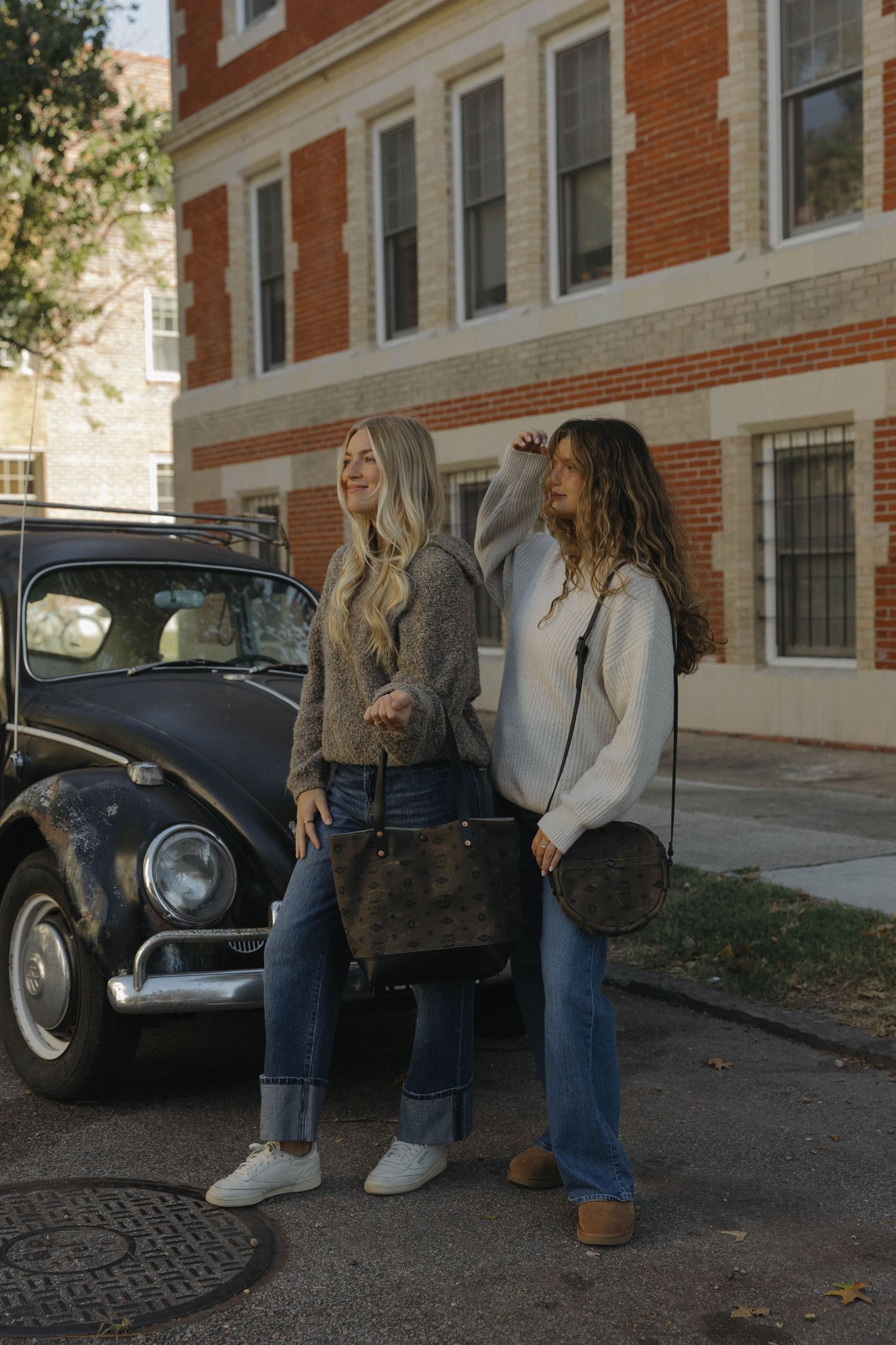 Students sitting together outdoors next to vintage black car on college campus grounds with red brick building.
