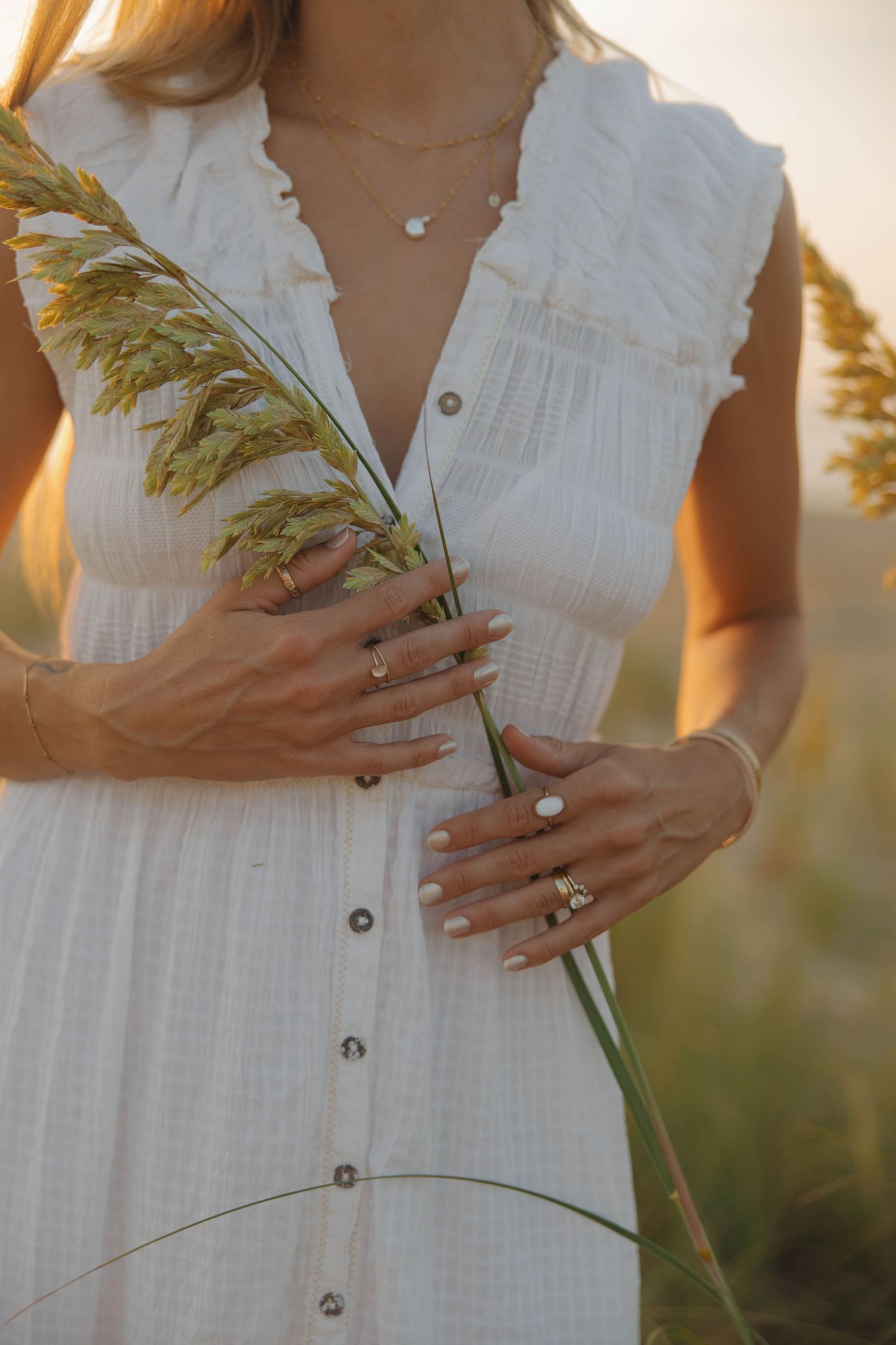 Close-up view of hands holding delicate wheat stalks against a white dress in golden sunset light.