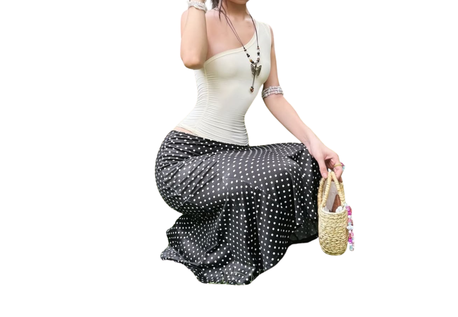 Woman wearing white top and black polka dot maxi skirt, holding a woven bag, posing against white background.