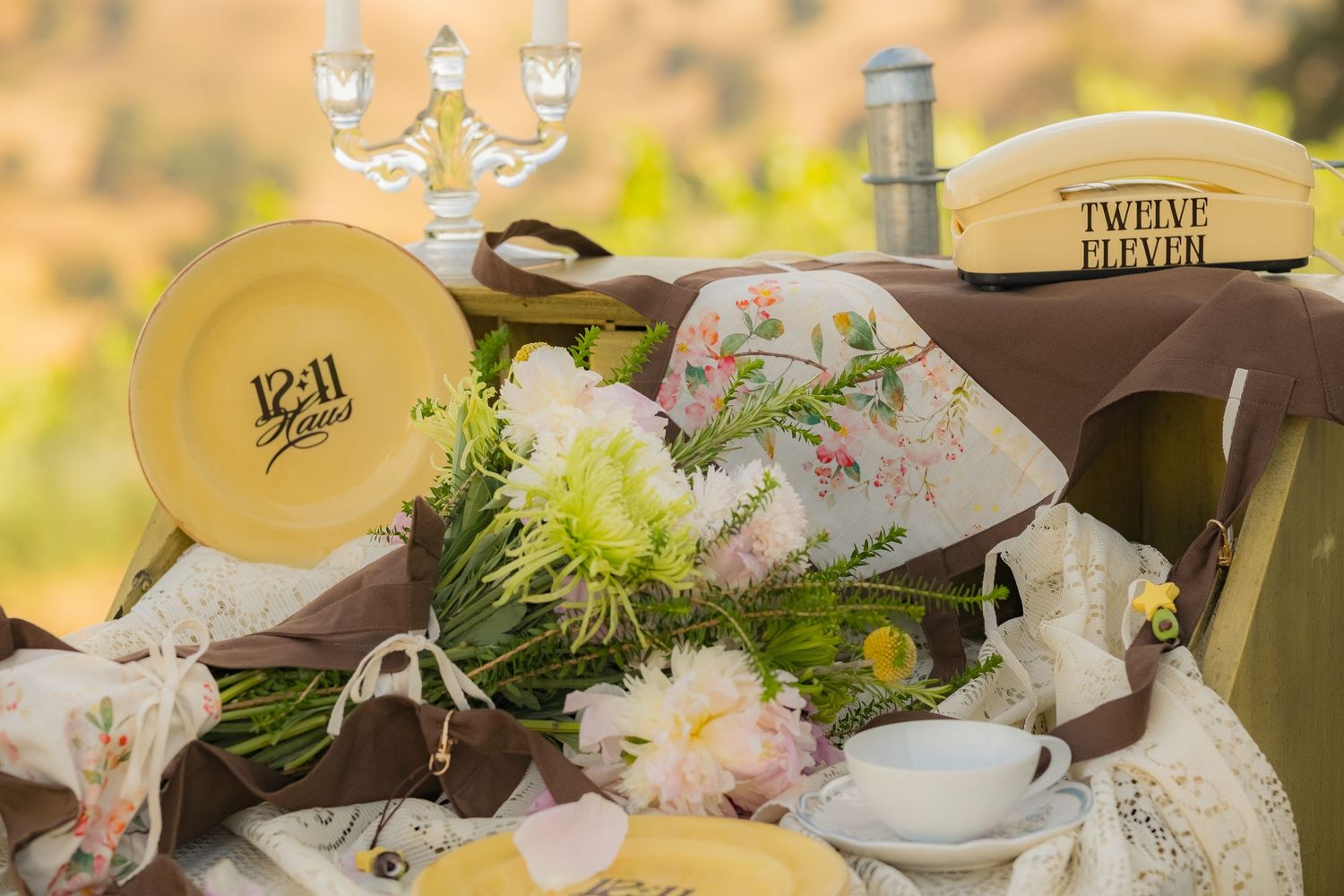 Vintage yellow dishes, floral arrangements, and antique decor styled on a rustic outdoor table setting.