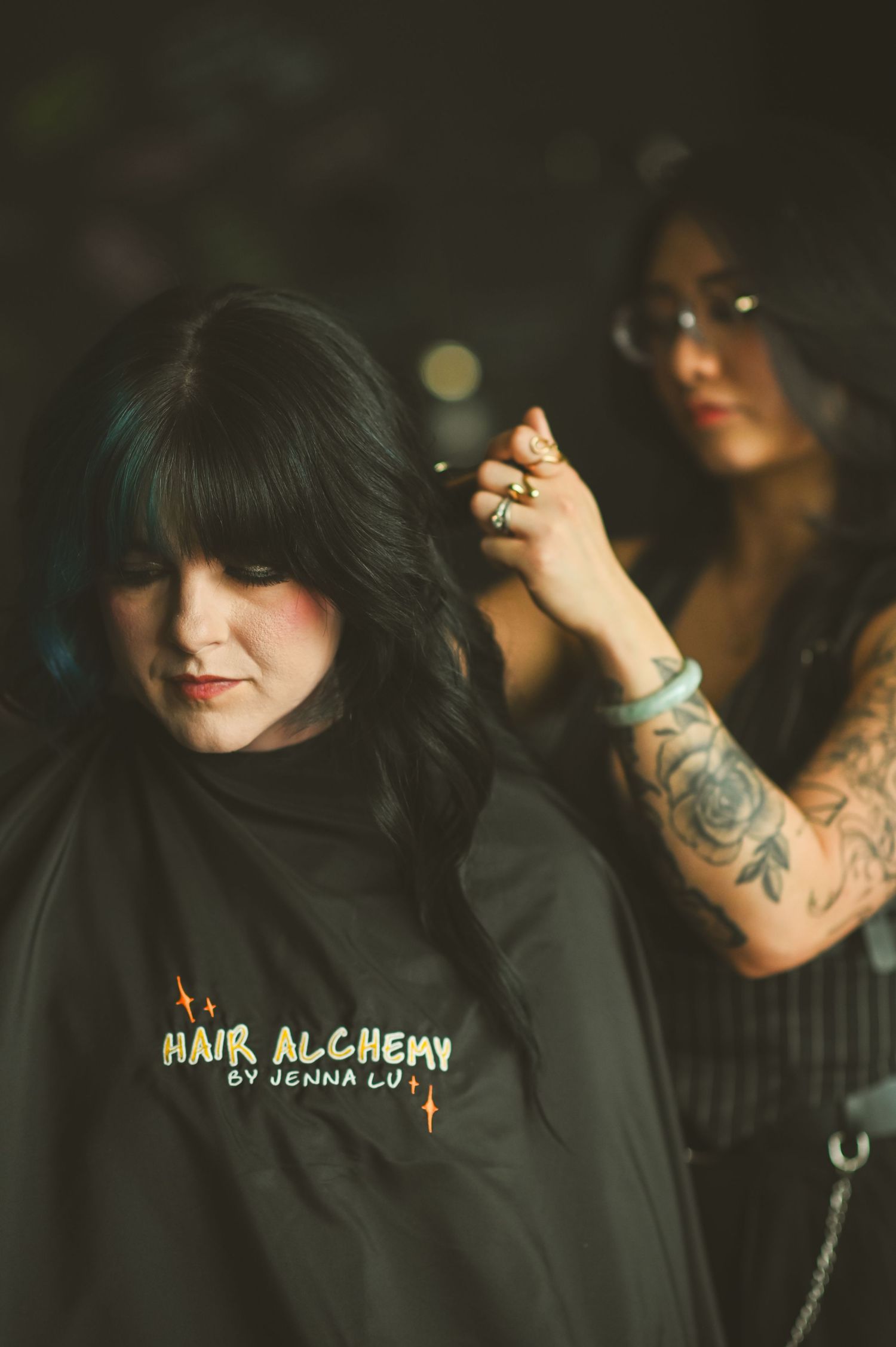 A client receives a hair styling service at Hair Alchemy salon while wearing a black cape.