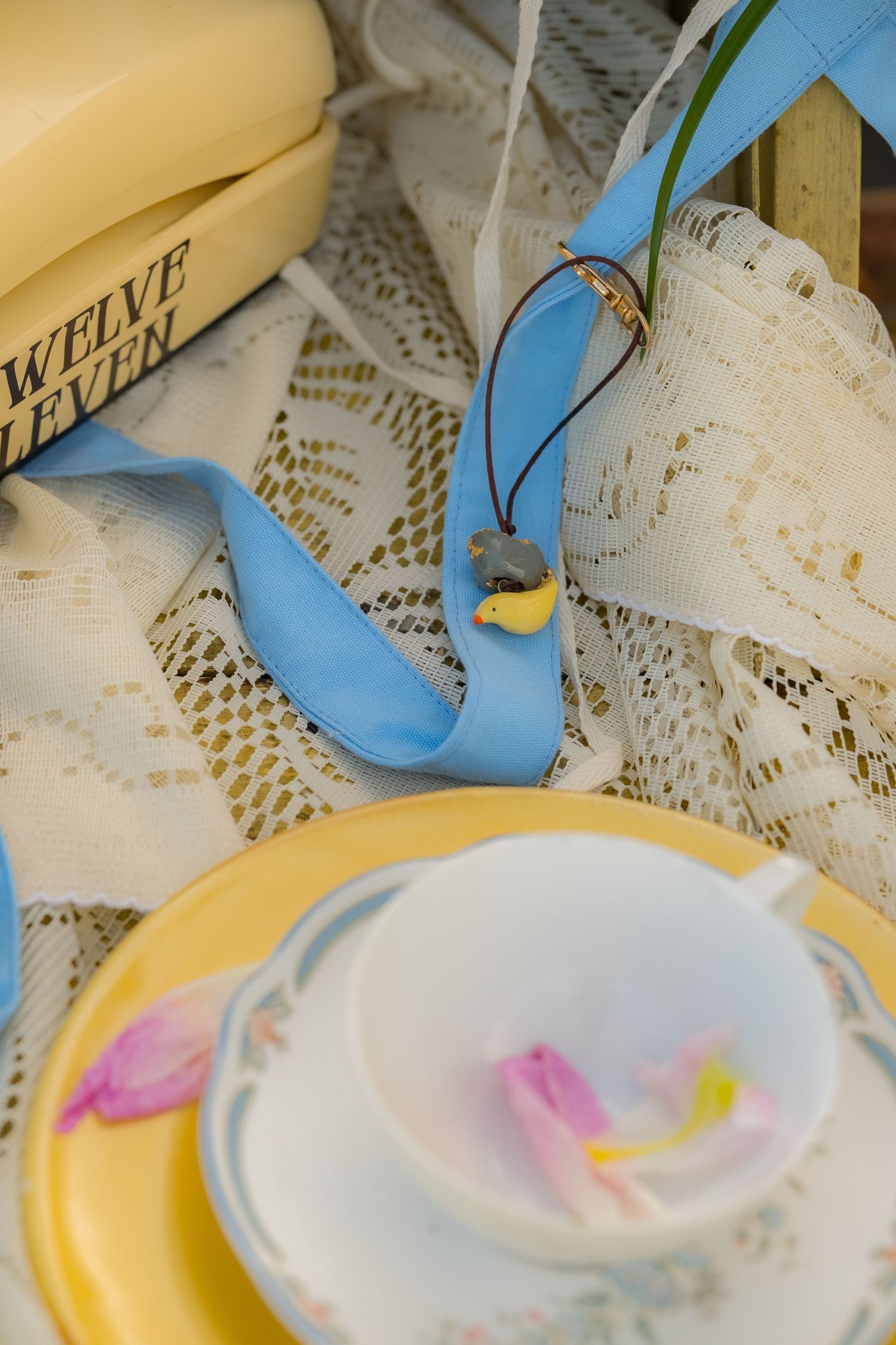 Vintage yellow phone, lace cloth, blue ribbon, ceramic teacup with tulip petals on yellow plate.