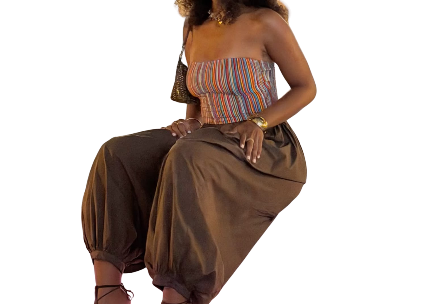 Woman wearing brown harem pants and a colorful striped strapless top, seated against a white background.