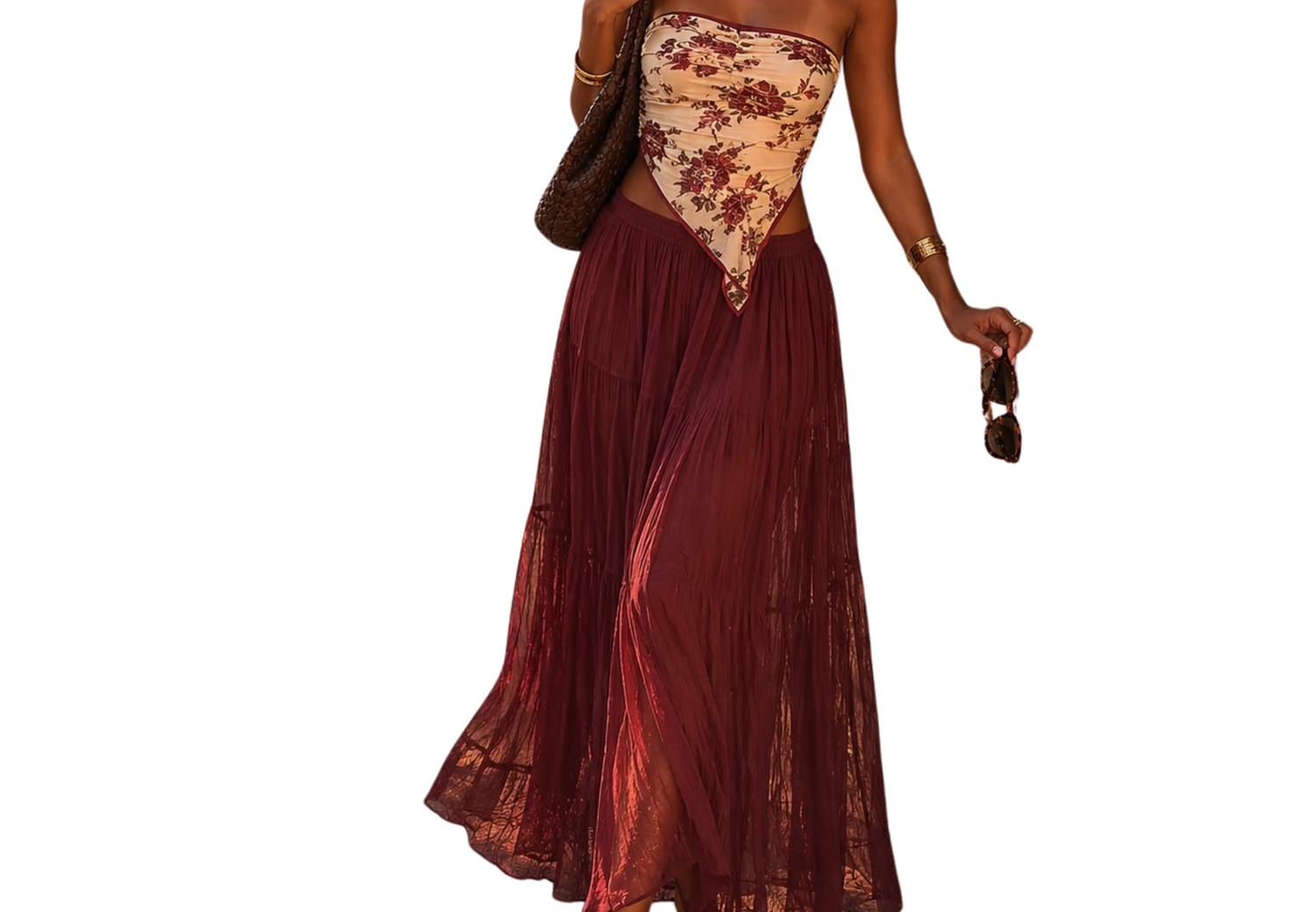 Woman wearing a strapless burgundy maxi dress with lace bodice detail, flowing pleated skirt, carrying a bag and sunglasses.