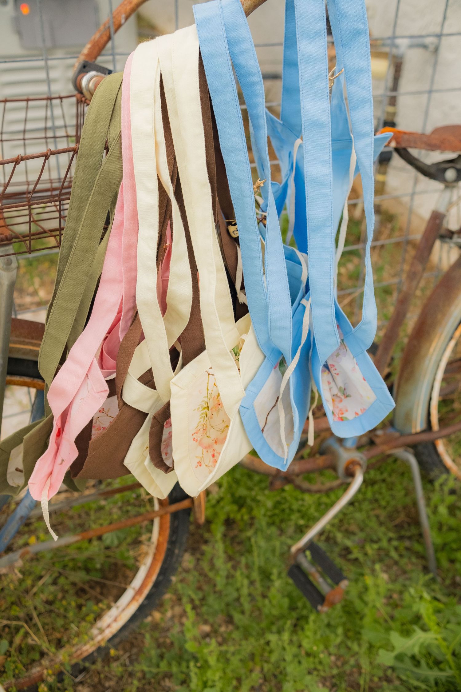 Colorful pastel ribbons and fabric strips hanging from a vintage rusty bicycle basket in an outdoor garden setting.