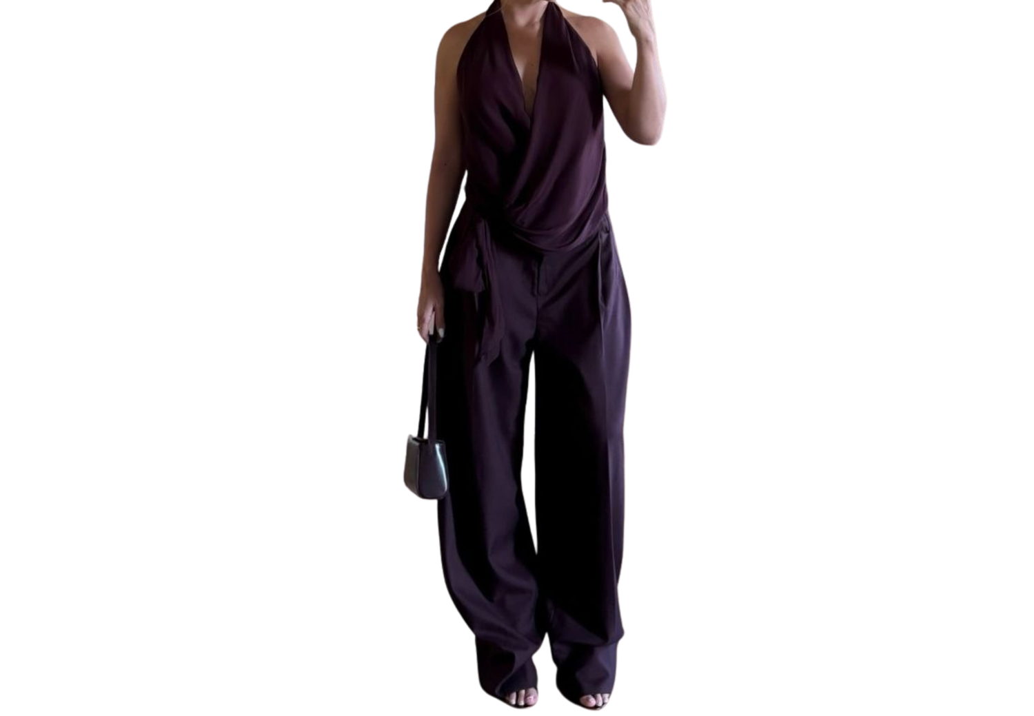 Dark purple halter jumpsuit with wide-leg pants, draped neckline, worn with strappy heels and small handbag.