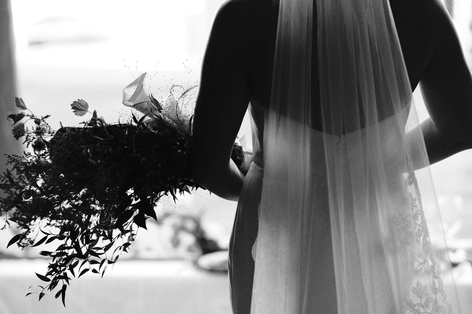 A silhouetted figure in a wedding dress and veil stands in front of a bright window creating a dramatic backlit effect.